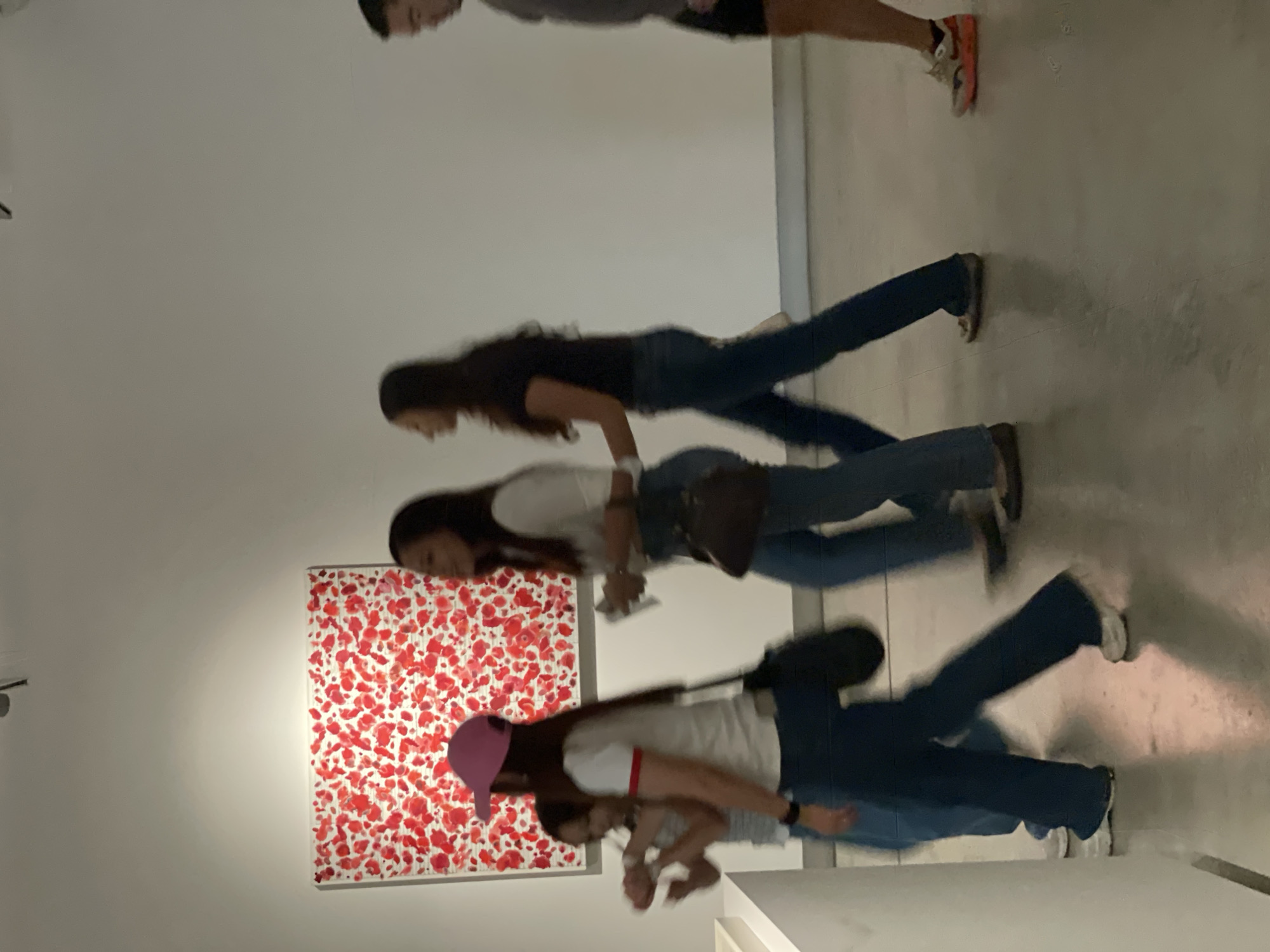 The image shows a group of people in an art gallery. There are at least four women visible, and a baby being held by one of the women. The women appear to be viewing a piece of art on the wall, a square painting with red and white abstract patterns. The background suggests a modern art gallery, with white walls and polished floors. It has been reported that the photograph was taken in Bangkok, Thailand.