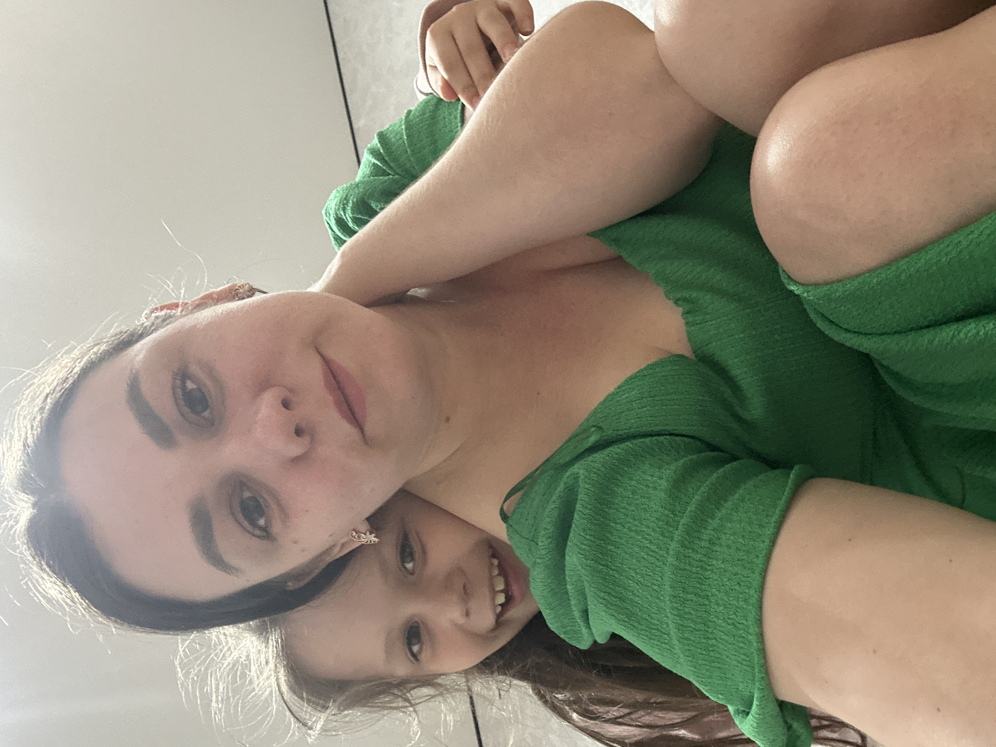 A selfie picture depicts a woman and a child, possibly a mother and daughter, wearing a green dress and standing indoors. The image appears to have been taken at an upward angle. There is no information available to determine if the photo was taken in Chaikovsky, Russia.