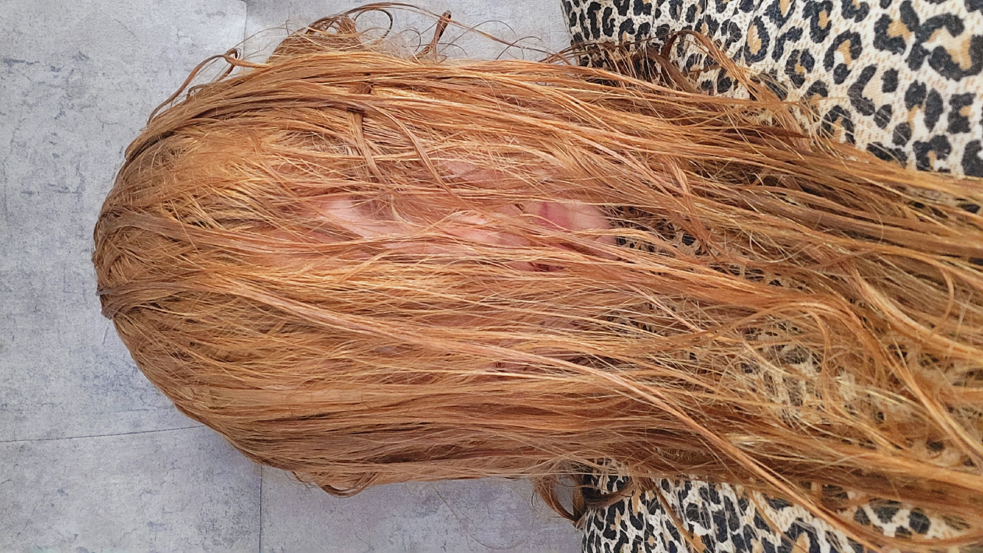 A person with long, wet, reddish-blonde hair is lying on a surface with their face obscured by their hair. Part of the person is on a surface with a leopard print design and part of the person is on a grey surface. No evidence suggests this image was taken in the city of Chaikovsky, Russia.