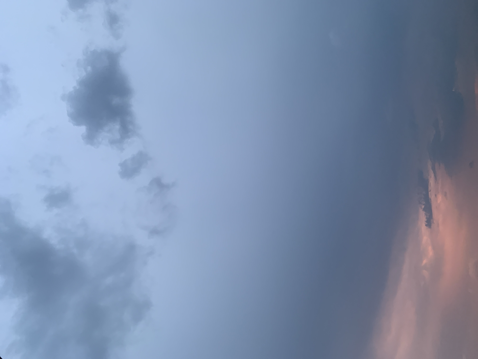 The image displays a cloud-filled sky, with no discernible landmarks or elements that would allow for specific localization to Kolomyia, Ukraine, or any other urban area. The composition consists of various shades of gray and blue clouds, with a subtle hint of pinkish hues at the bottom left, suggesting either a sunset or sunrise. The lighting is diffused, indicating overcast conditions or twilight. No people, subjects, objects, or actions are visible. The environment is solely the sky.