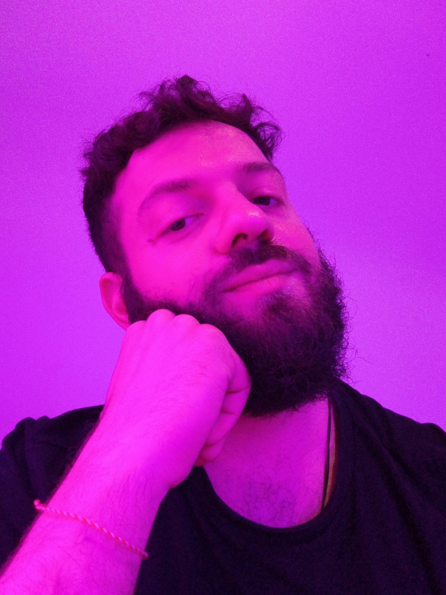 A man with dark, curly hair and a full beard rests his chin on his fist. He is wearing a dark t-shirt and a bracelet is visible on his wrist. The scene is lit with a strong purple hue, casting the background and subject in a uniform violet color. There is no evidence available to ascertain that the location of this image is in Diepholz, Germany.