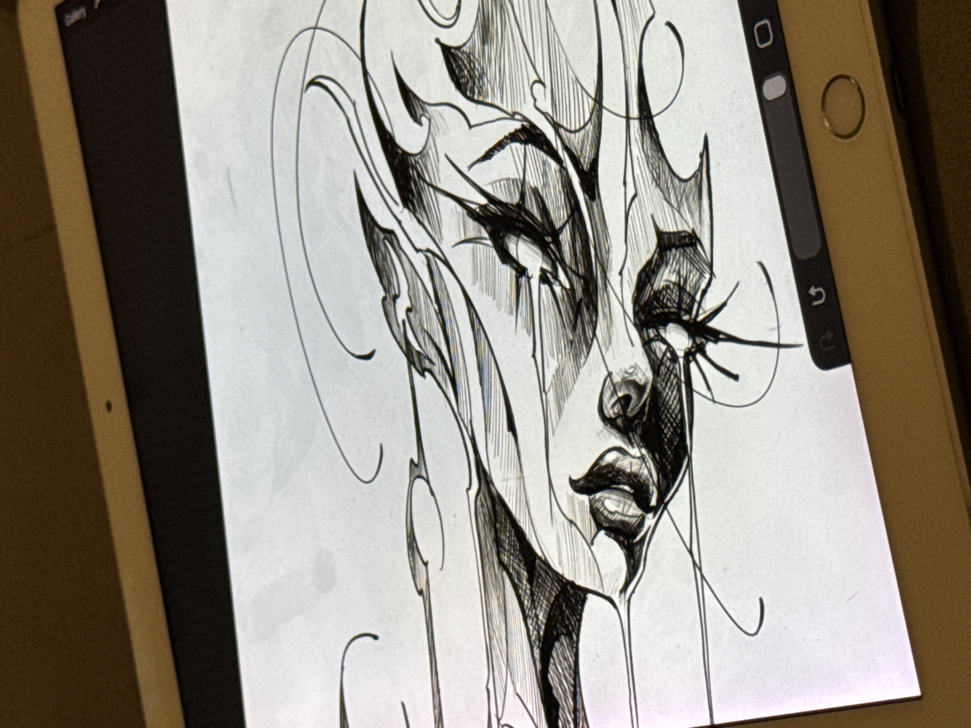 A gold-colored Apple iPad is presented at an angle, viewed from above and slightly to the right, resting on an unidentifiable dark brown surface. The tablet's screen displays a digital drawing in a monochrome palette, featuring intricate black line art and cross-hatching for shading. The artwork depicts highly stylized, organic forms reminiscent of fantastical creatures or elaborate decorative motifs, characterized by sharp angles, flowing curves, and dense areas of black fill. Elements suggestive of wings, fins, and abstract skeletal structures are visible within the composition. The user interface of a drawing application is partially discernible at the bottom right, showing icons for undo and redo, along with a tool selection area. A "Gallery" option is also visible in the top right corner of the application. Although the image itself lacks specific geographical indicators, the scene is contextually located in the city of Sofia, Bulgaria.