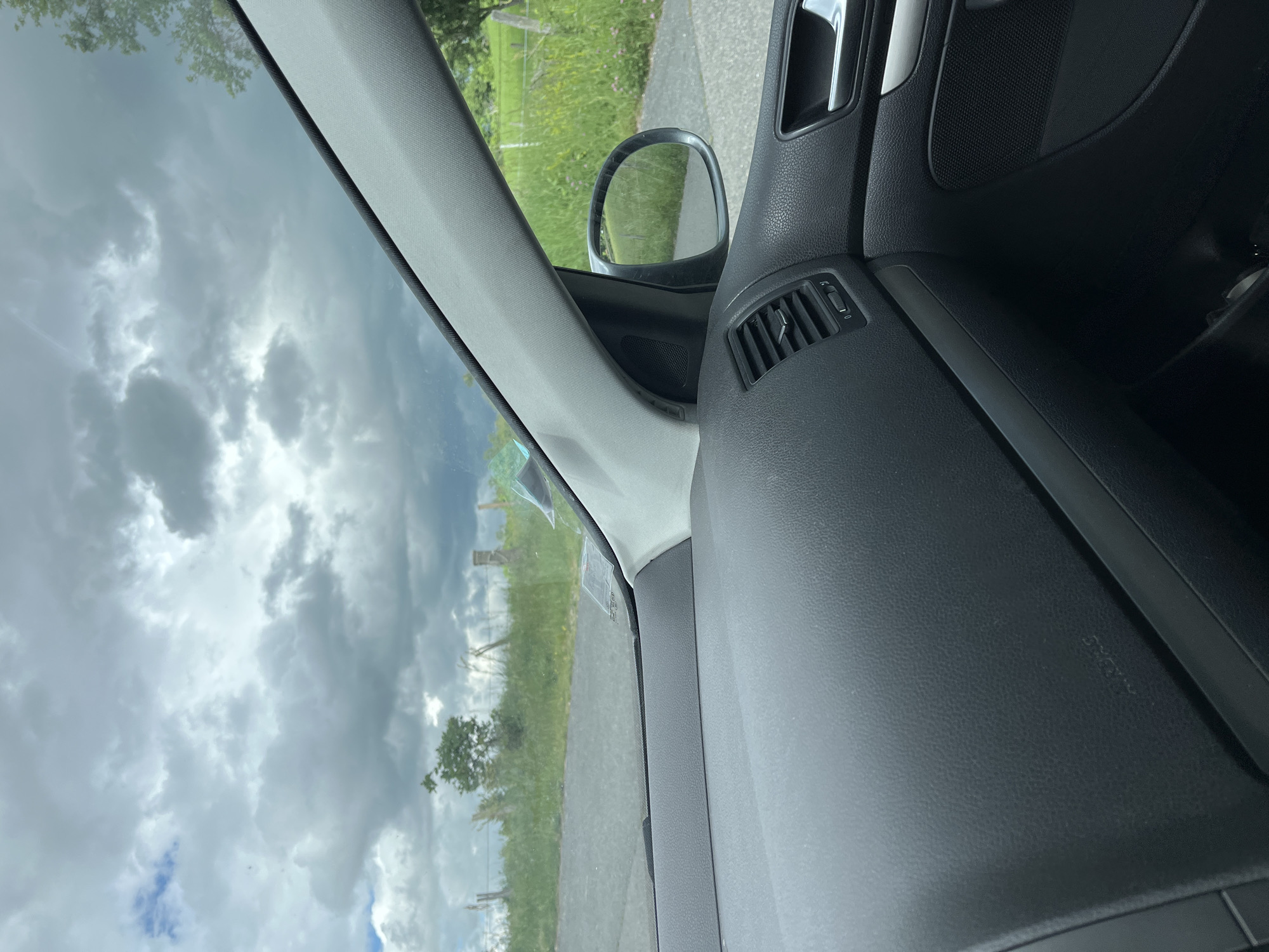 The image shows a view from inside a car. The windshield reflects a cloudy sky. The side view mirror and part of the car's interior, including the dashboard and door panel, are visible. The outside scene includes a grassy area and a road. There's no indication of people, actions or interactions. It's not possible to confirm if this is indeed Chambœuf, France.