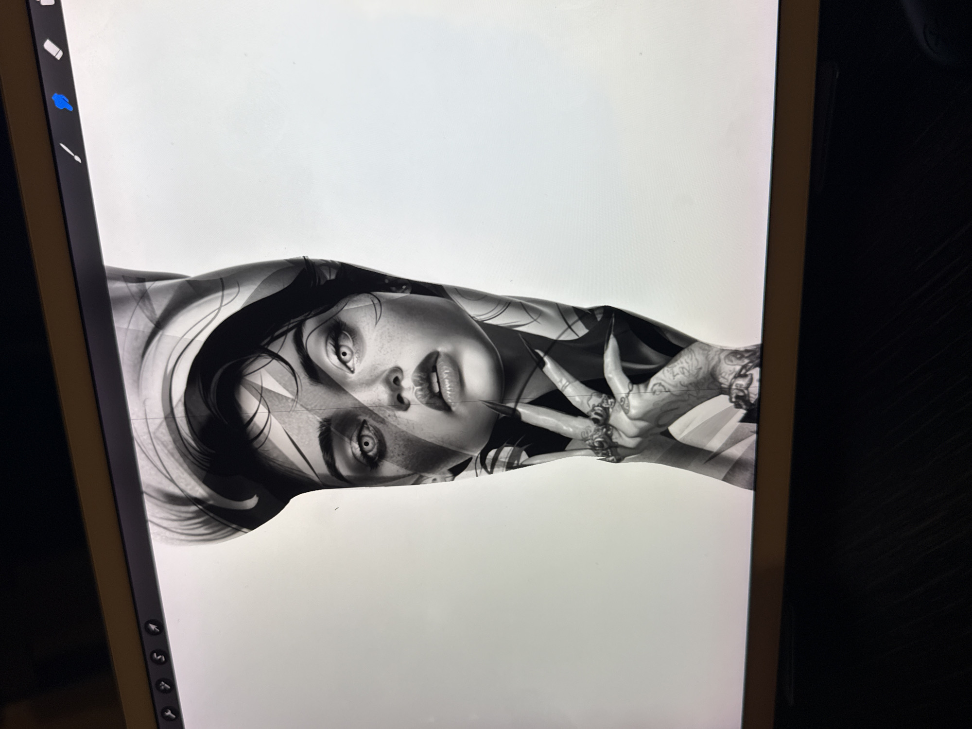 The image depicts a digital drawing of a woman's face and part of her upper body on a tablet screen. The artwork is black and white and appears to be a detailed illustration or tattoo design. The woman has a captivating gaze, defined features, and intricate details in her hair and skin. Her hands are positioned near her face, adorned with rings and tattoos. The background is a plain white digital canvas. The scene is inside, with part of a dark surface visible to the right of the tablet. The image does not contain any information about the city of Sofia, Bulgaria.