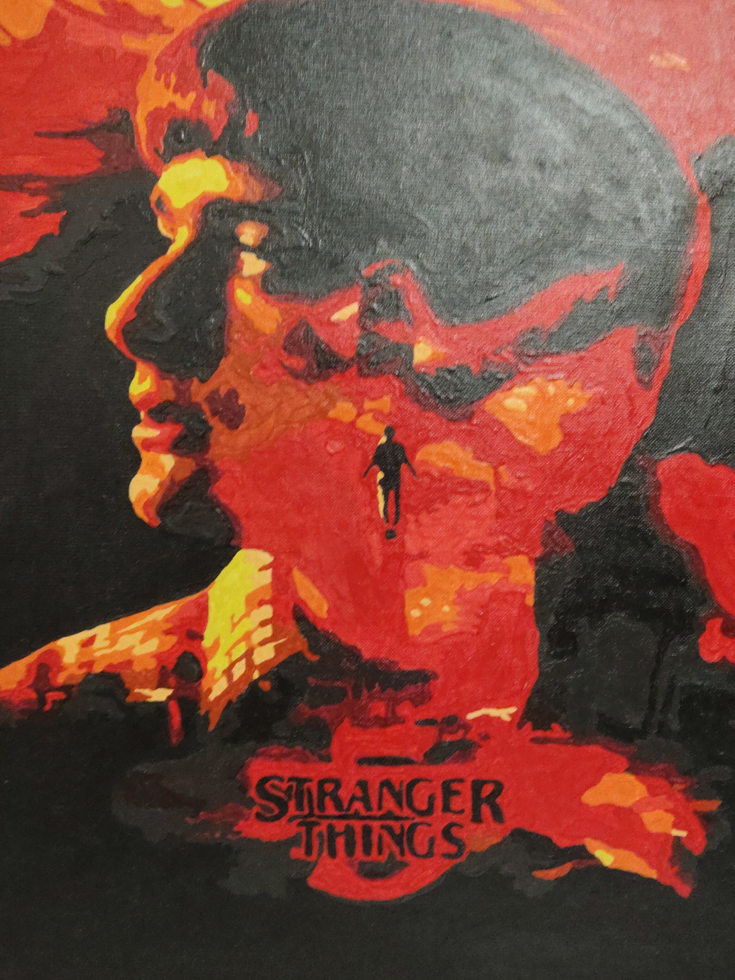 The image is a painting in shades of red, orange, and black, depicting a profile of a person. Inside the person's silhouette is a small figure standing on a reddish surface. At the bottom of the painting, the words "STRANGER THINGS" are written in red. The background of the painting is black. The location of the image is unknown.