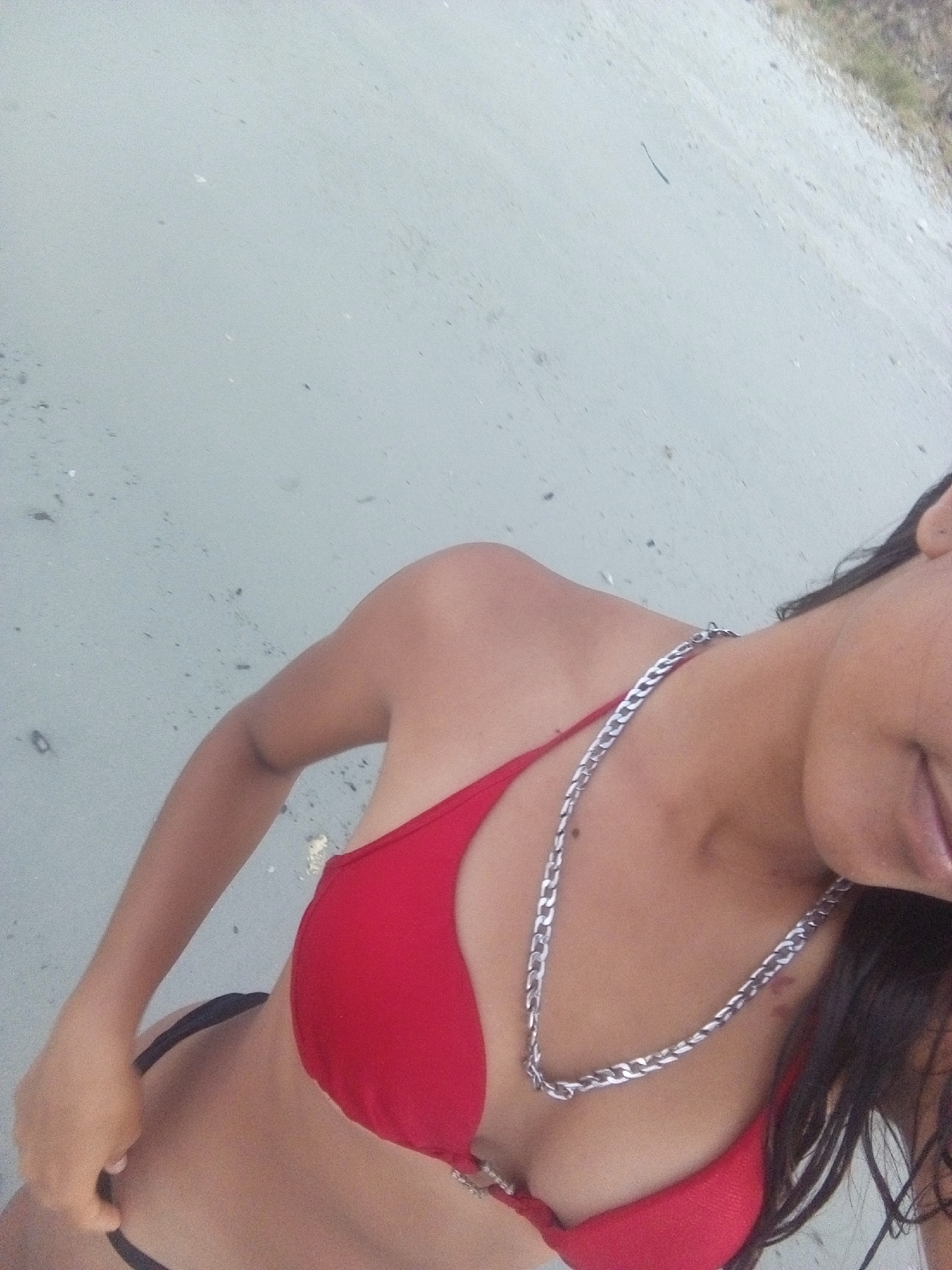 A woman wearing a red bikini and a silver chain is on a beach. The background is blurred and appears to be sand. The location is possibly near the city of Juan Griego, Venezuela.
