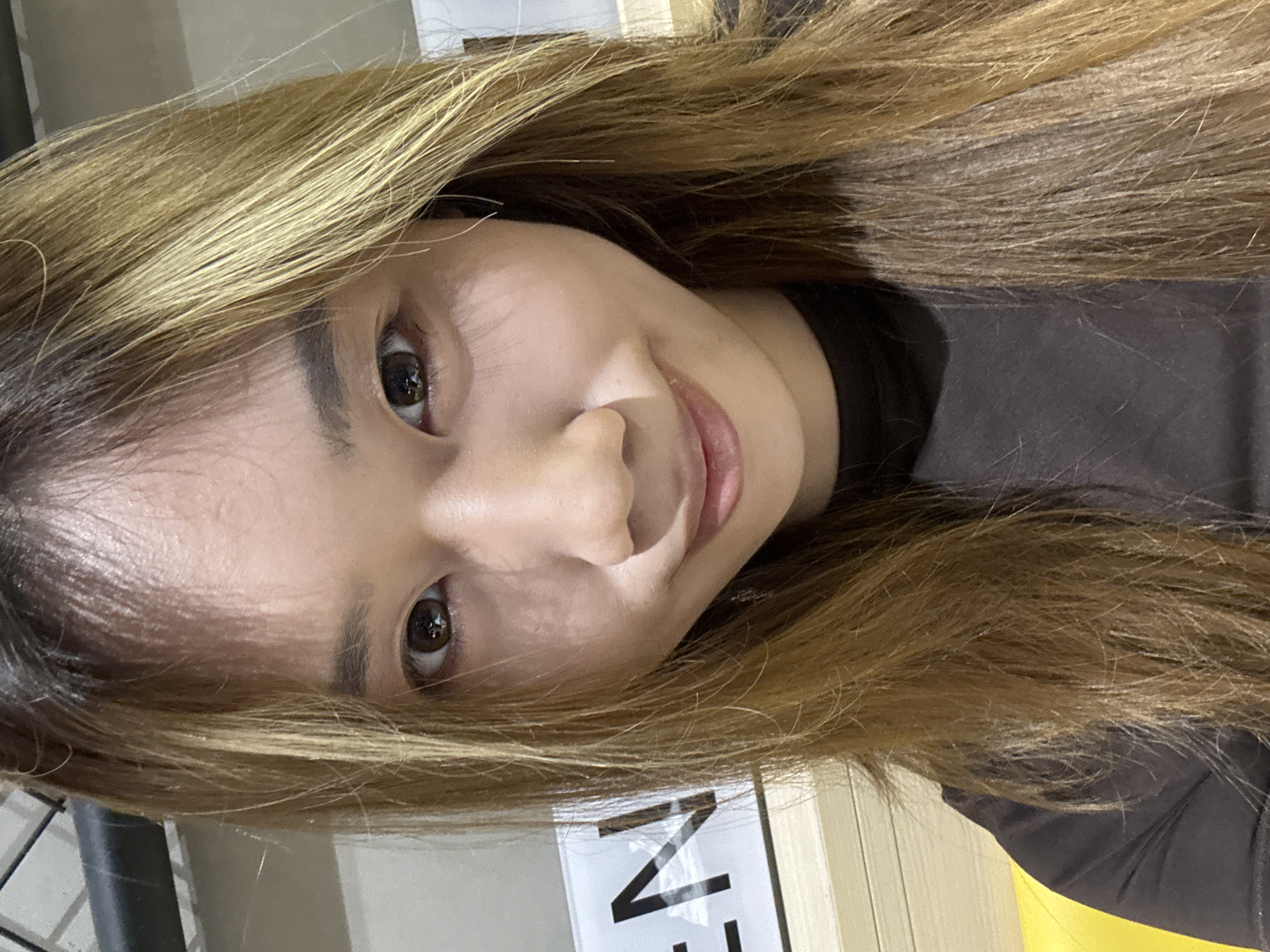 A close-up, slightly rotated selfie of a woman with light brown hair. She is wearing a dark top. The background is blurred, with hints of white and yellow surfaces. It is not possible to confirm this image was taken in Yuzhong District, China based on provided information.