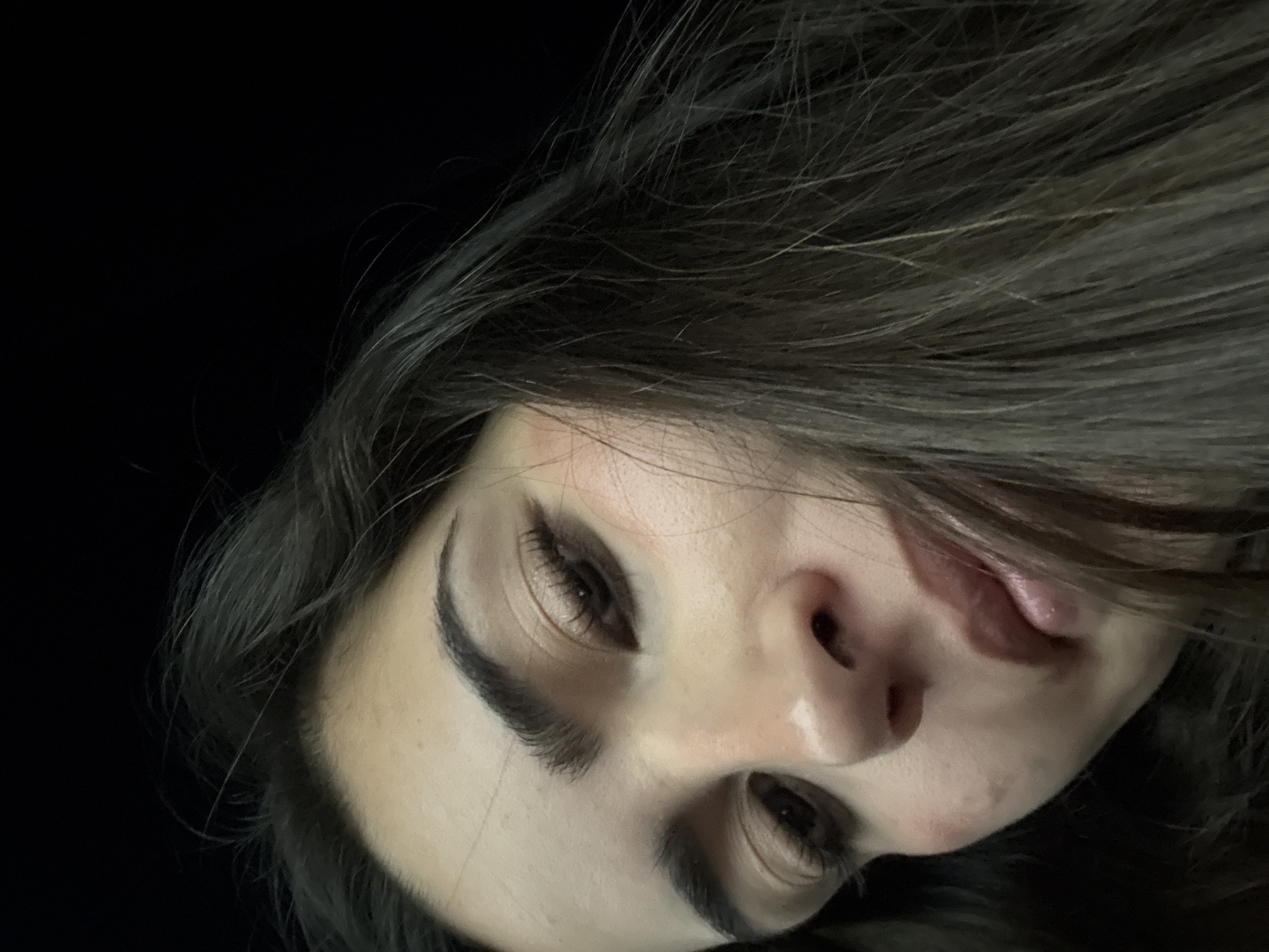 A close-up, low-angle shot of a person's face. The person has fair skin, dark eyebrows, and dark hair. The person's eyes are partially closed and angled downwards. The nose and mouth are prominent features. The background is dark and indistinct. The location is unspecified and there is no indication it is in San Bernardino Tlaxcalancingo, Mexico.