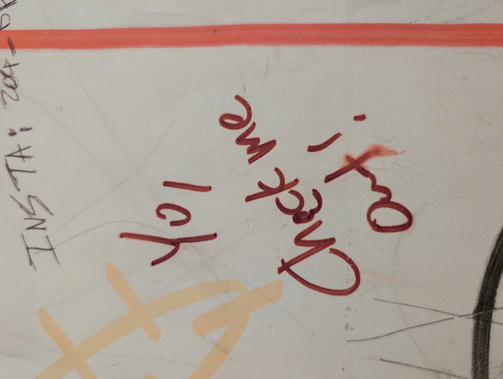 The image depicts a section of a wall covered in graffiti. The wall appears to be off-white. A thick orange-red line runs horizontally across the upper portion of the image. A message in dark red marker reads "Check me out!" next to "lol". To the left, the partial phrase "INSTA+ 2004" is written in black ink. Other yellow-orange scribbles are present. The presence of the graffiti suggests an urban environment, however, there is no information regarding its location in Paris, France.