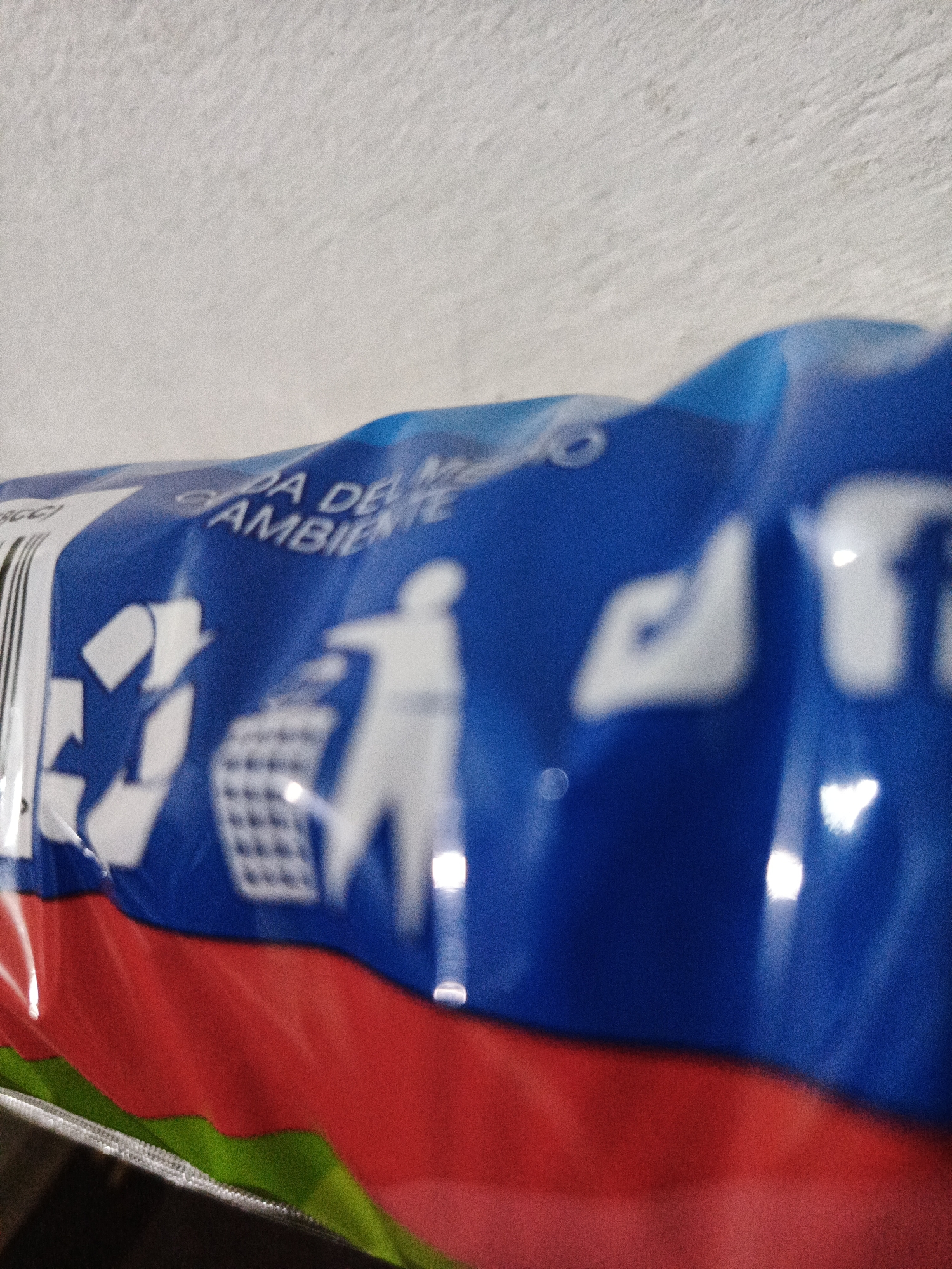 A close-up shot of a blue, red, and green package. The package has recycling symbols and a person throwing something in a trash can. The words "A DE" and "AMBIENTE" are visible. The image appears to be taken indoors with a blurry, white background. The specific location in Los Robles, Venezuela, cannot be determined.