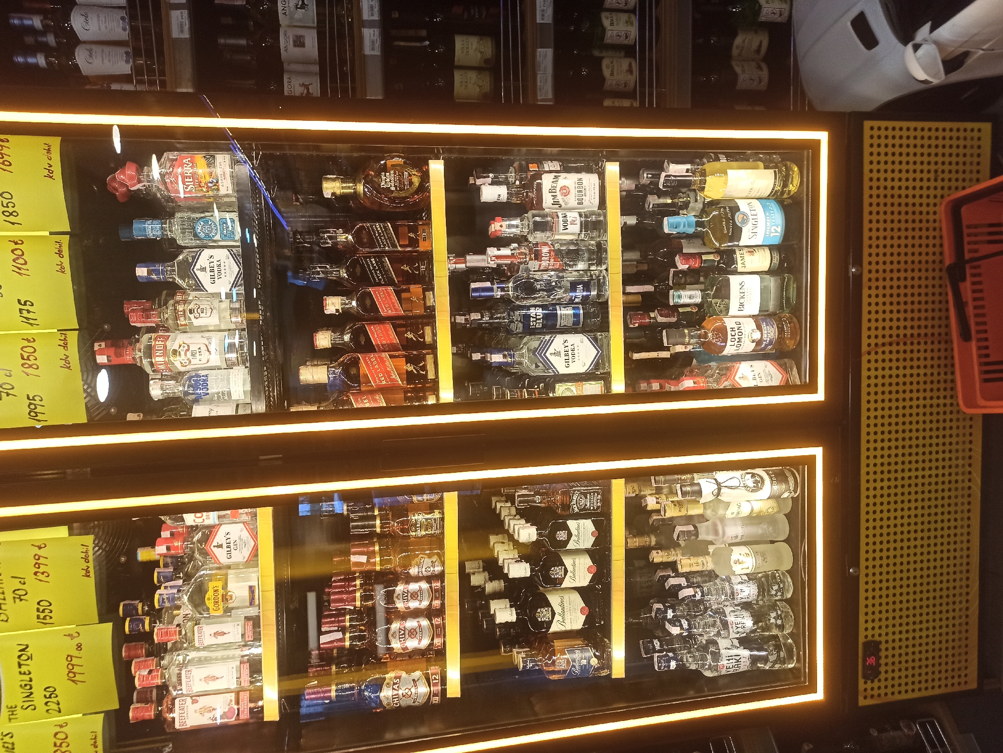 The image shows a refrigerated display of alcoholic beverages in a store. The display is brightly lit with yellow LED lights. On the top shelf of the left display, there are bottles of Johnnie Walker Red Label, Johnnie Walker Black Label, and another bottle of Johnnie Walker. Below that, on the second shelf, are bottles of Chivas Regal 12 Year Old. On the third shelf, there are bottles of Ballantine's and Jack Daniel's. The bottom shelf shows various bottles of clear spirits, including some that appear to be vodka. The right display has bottles of Gilbey's Vodka, Smirnoff, Sierra Tequila, and other brands. There are also bottles of Gin and Bourbon visible. The background of the store is dimly lit. The store appears to be in Ümraniye, Turkey, based on a price tag in the top left corner that reads "1999.00 t", with "t" likely referring to Turkish Lira. There are no people visible in the image.