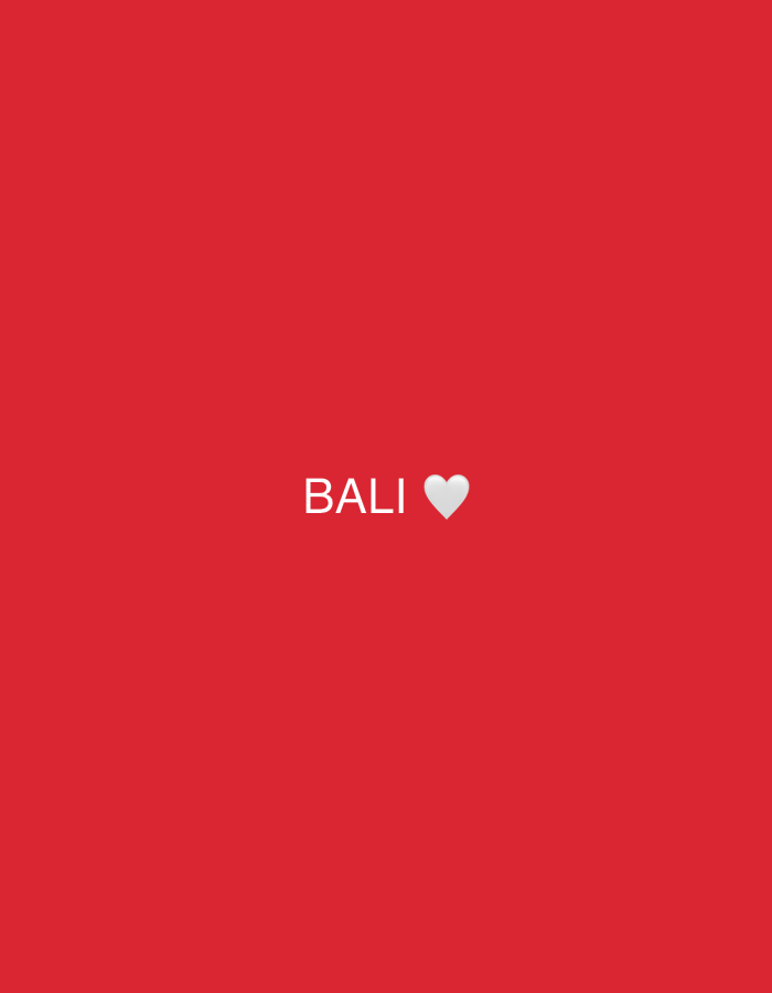 The image displays a minimalist composition featuring white text and an emoji centered against a solid, vibrant red background. The text reads "BALI" in uppercase sans-serif font, immediately followed by a white heart emoji. There are no people, objects, or discernible scene elements present. The red background is uniform, lacking any textures or patterns. No specific activity or event is depicted. The overall impression is one of simplicity and direct communication, likely conveying affection or a positive sentiment towards Bali, which aligns with the given location context of North Kuta, Indonesia. The time of day and weather are not indicated.