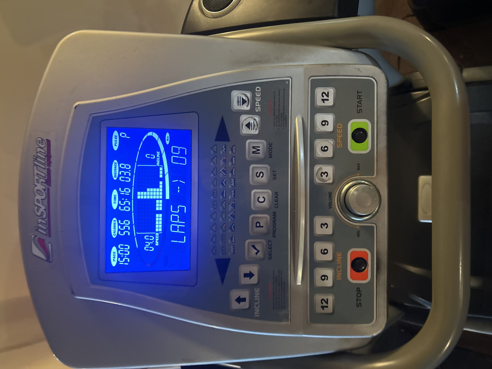 The image shows the console of an inSPORTline treadmill. The screen displays a workout in progress, with data showing pace at 15:00, calories burned at 556, workout time at 65:16, distance traveled at 03.8, pulse indicated, speed at 04.0, incline at 0, and laps at 09. The control panel includes buttons for speed and incline adjustment, program selection, clear, set, mode, start/stop, and volume. There are quick-select buttons for speed (3, 6, 9, 12) and incline (3, 6, 9, 12). The console is made of gray plastic. The treadmill handles are light beige. The location in Elhovo, Bulgaria, is not determined from the image.
