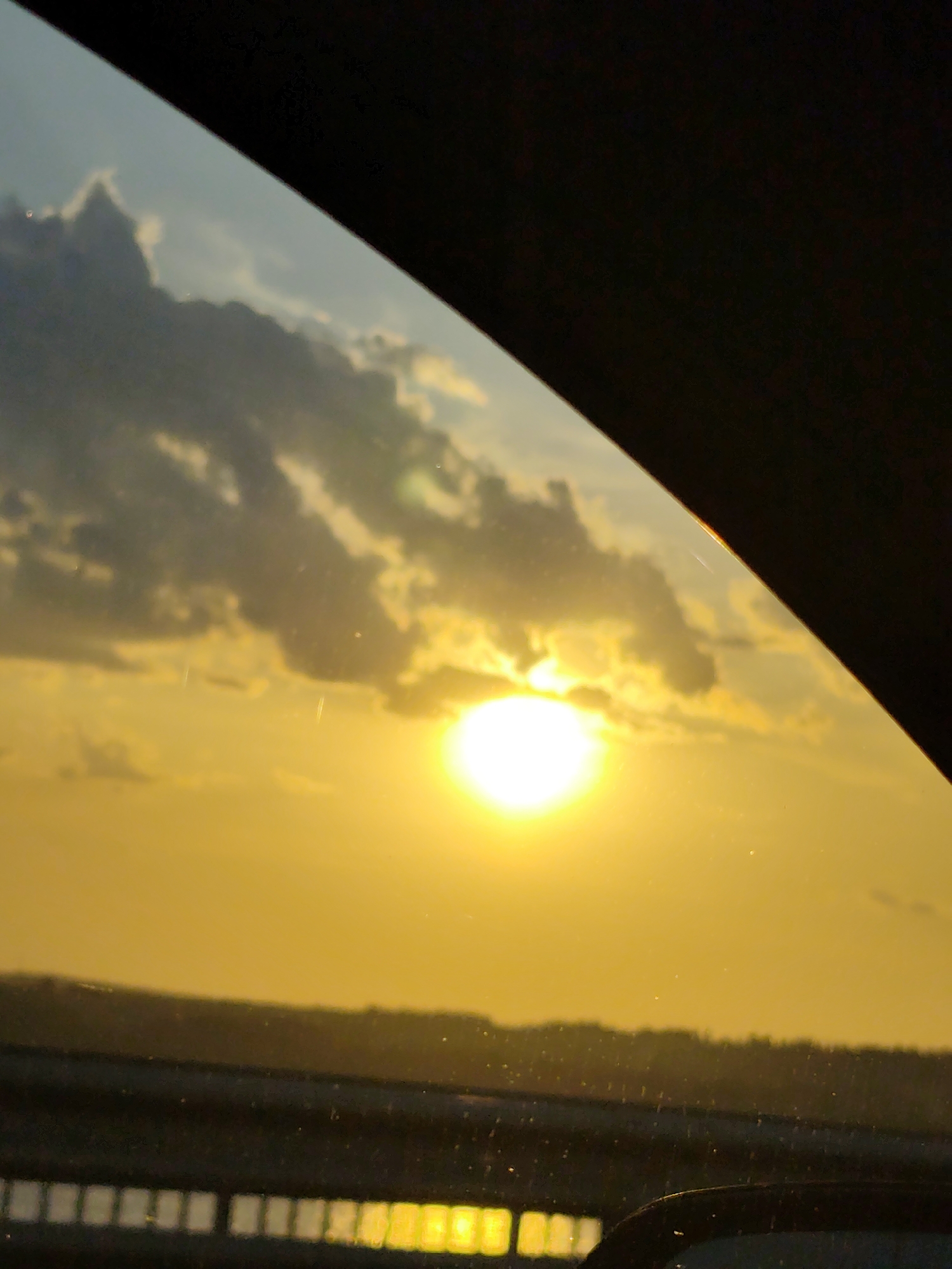 View of a sunset with clouds through a car window. The location is not evident from the image.