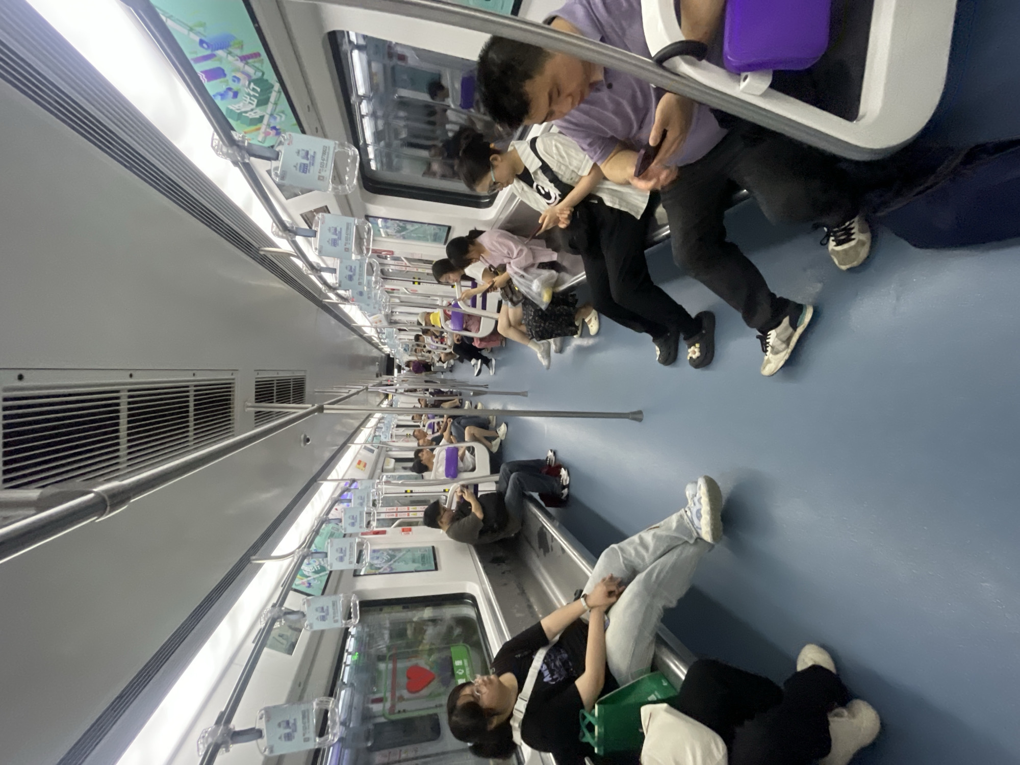 The image depicts the interior of a subway car in Yuzhong District, China. Passengers are seated along the sides of the car. Some passengers are looking at their phones. One passenger is reclining across the floor. Overhead advertisements are visible. The floor is light blue, and the car appears to be relatively clean.