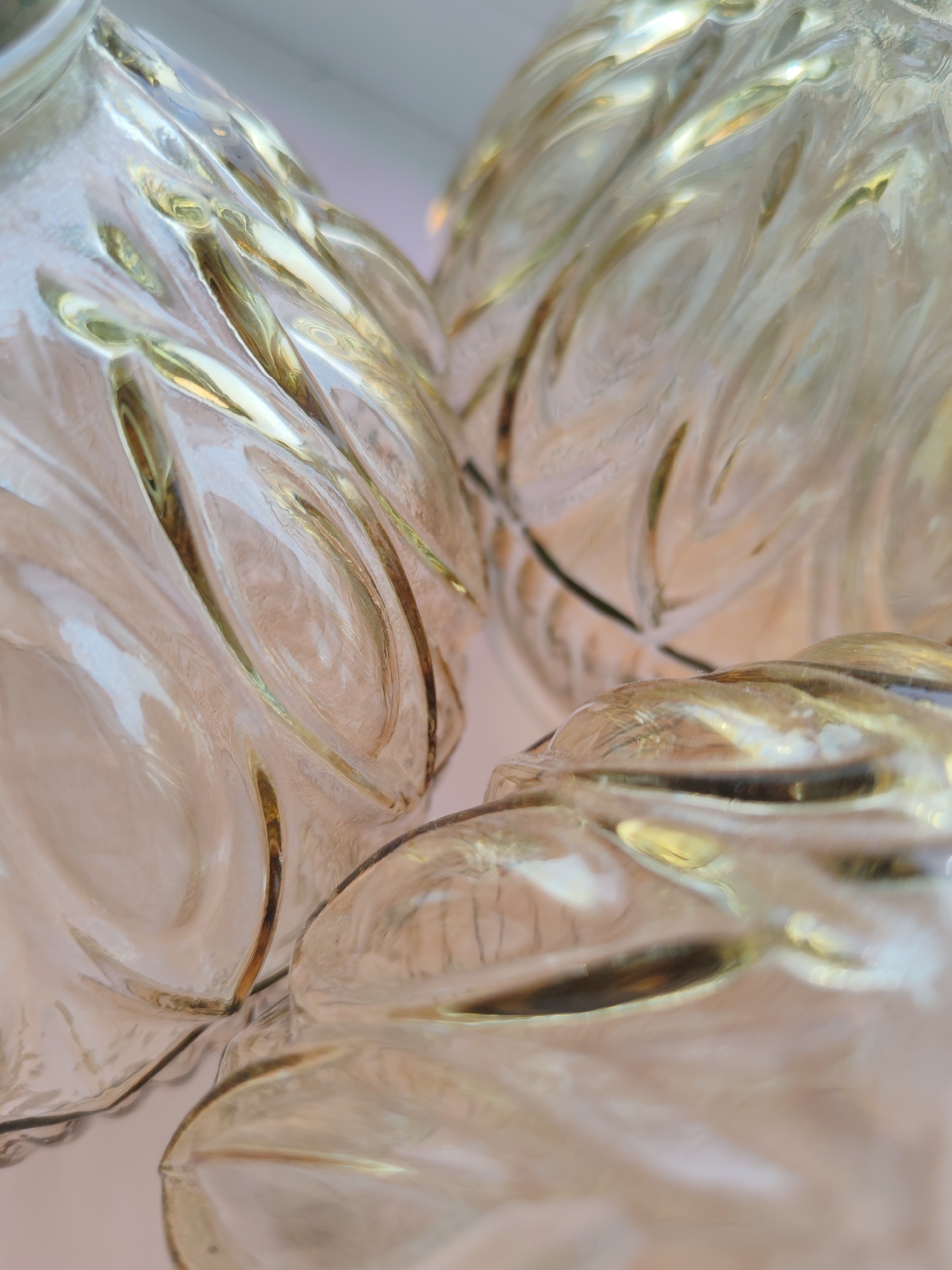 The image shows a close-up of three intertwined glass objects with a swirling, patterned design that features golden accents. The shapes are rounded and partially obscured by the tight framing of the shot. The background appears to be a muted, light color, possibly a wall or ceiling. There are no people visible in the image. There is no information in the image that specifies this is taken in Ust-Ilimsk, Russia, therefore the location is unknown.