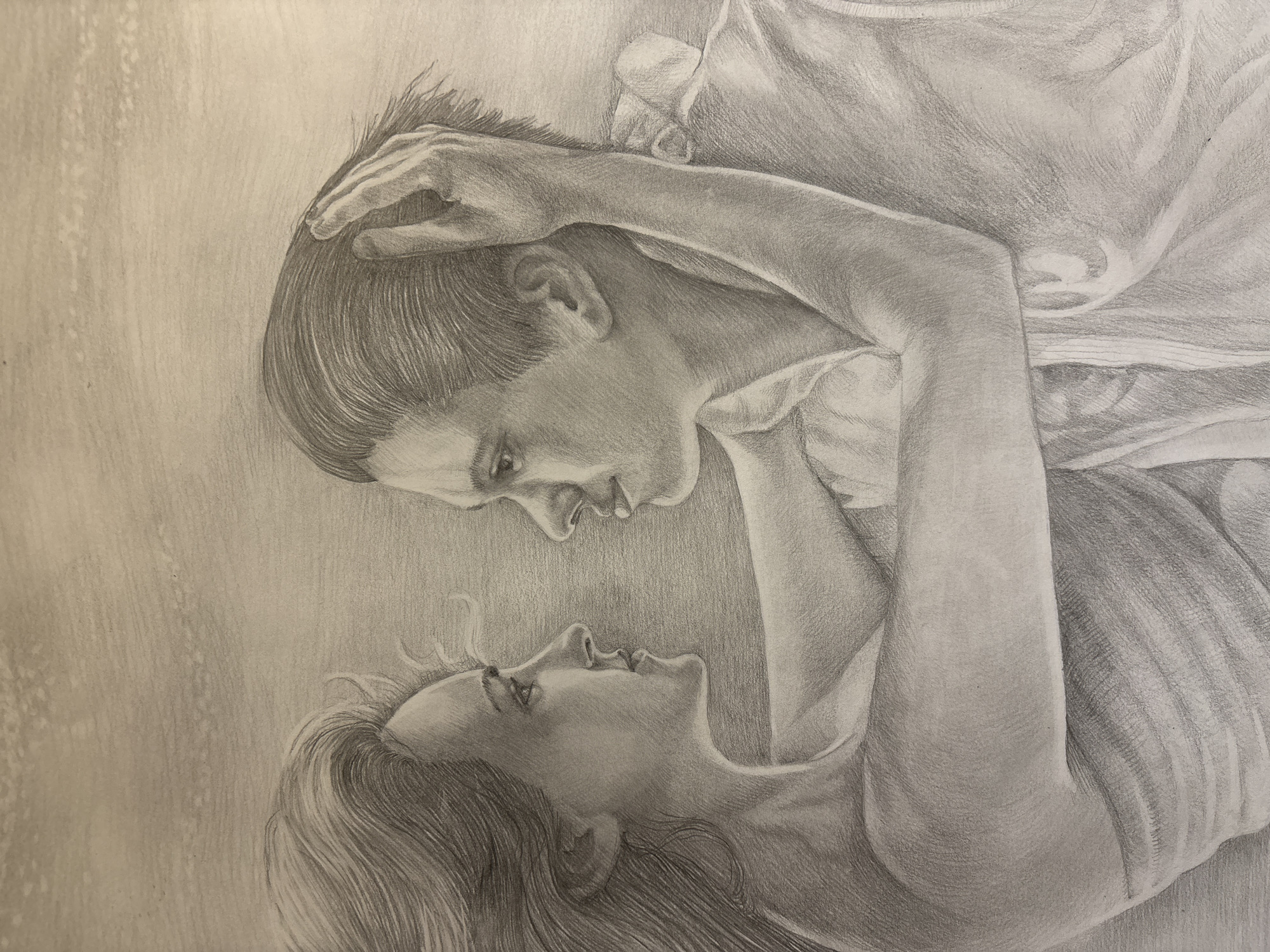 A monochrome pencil drawing depicts two individuals, appearing to be a man and a woman, in an intimate embrace. The figures are positioned diagonally, with the man's head and upper body in the upper left section, looking down, and the woman's head and upper body in the lower right, looking up. Their faces are very close, and their eyes are locked in a gaze that suggests tenderness or deep affection. The man's right hand is gently placed on the woman's head or hair, while his left arm is bent upwards. The woman's hair flows downwards from her head, and her left arm is bent. Both are depicted wearing clothing, with visible folds and textures rendered through detailed shading. The background is simple and unadorned, allowing the focus to remain entirely on the interacting figures. There is no visible text. The drawing showcases realistic rendering of features, hair, and fabric. The overall scene conveys a powerful emotional connection between the two subjects.