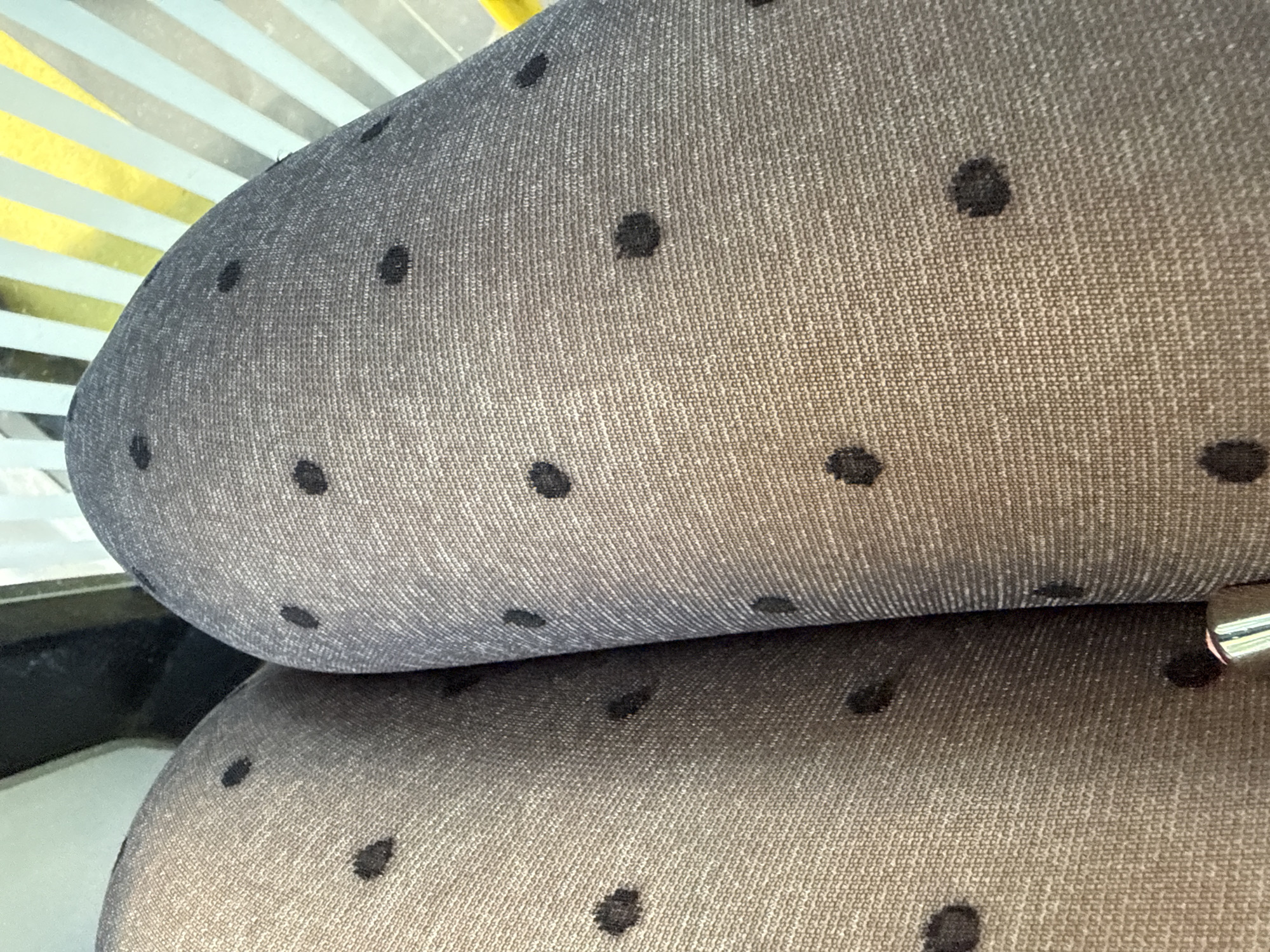 The image shows a close-up of a gray, fabric-covered surface with black polka dots. The fabric appears to be stretched over a curved form, possibly part of a chair or seat. There are no people visible, and the location is unknown.