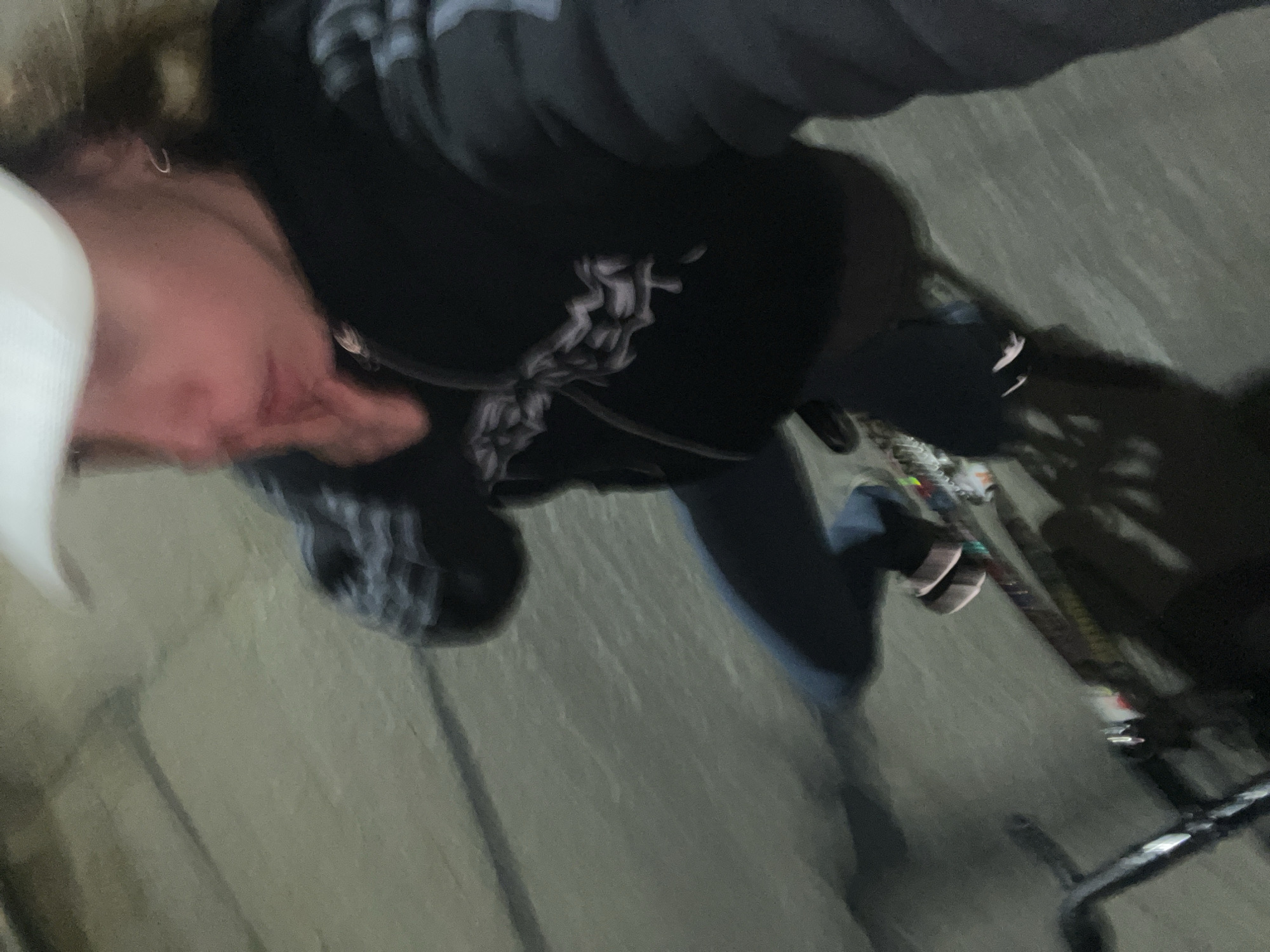 A blurry image shows a person wearing a white cap, dark hooded sweatshirt with a graphic design on the chest, and jeans. They are standing next to a bicycle on what appears to be a paved surface. The location is possibly Olivos, Argentina.