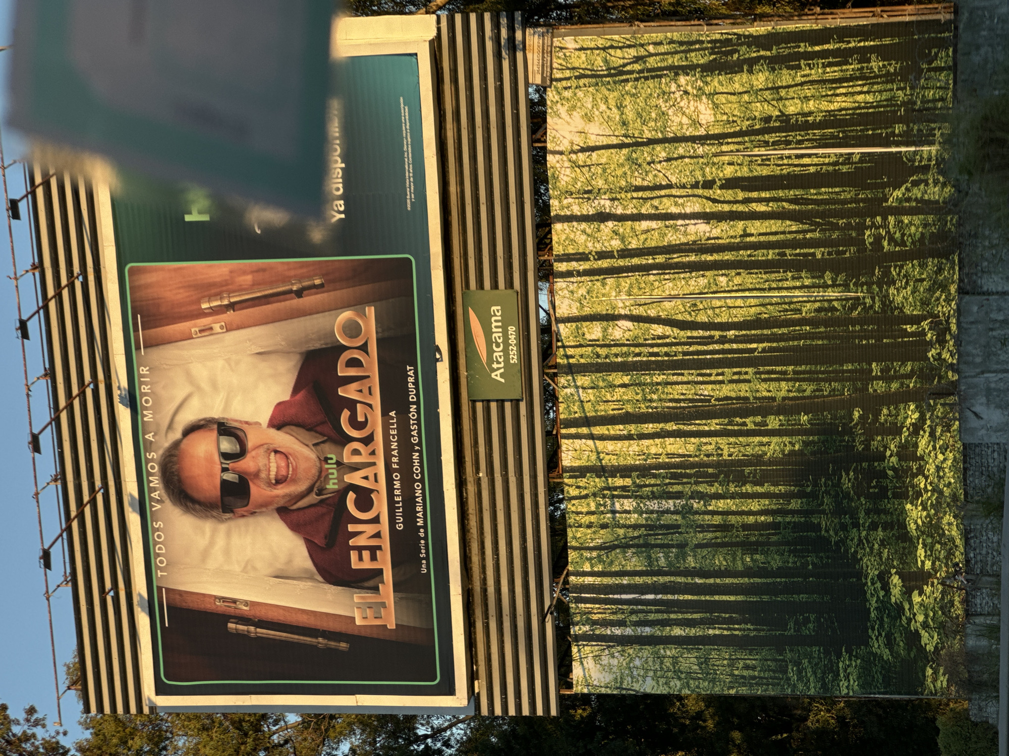 The image shows a billboard advertising the Hulu series "El Encargado", starring Guillermo Francella. The billboard is located in the city of Buenos Aires, Argentina. Adjacent to it is another billboard with a forest theme.