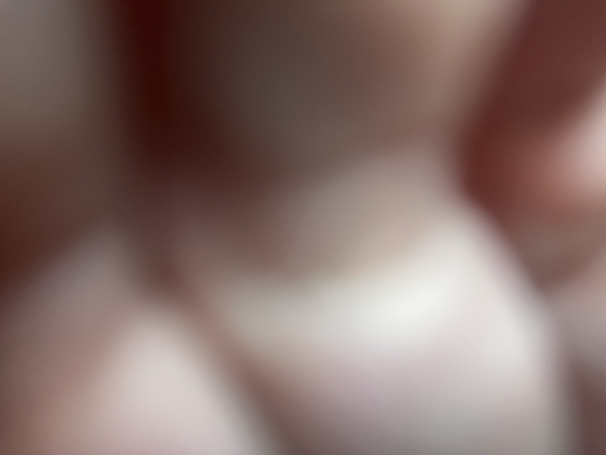 The image is a close-up, abstract, and out-of-focus shot of what appears to be skin. The colors are muted, with soft gradients of light pink, beige, and dark brown, suggesting a warm and possibly intimate setting. The blurred shapes create a sense of depth and texture, but offer no specific identifiable features of a person, object, or scene. There is no discernible activity or event taking place. The lighting is soft and diffused, with areas of bright highlight and shadow, but no clear indication of the time of day or specific location. There is no visible text in the image. The abstract nature of the image prevents any specific emotional interpretation or identification of location cues within Belgrade, Serbia.