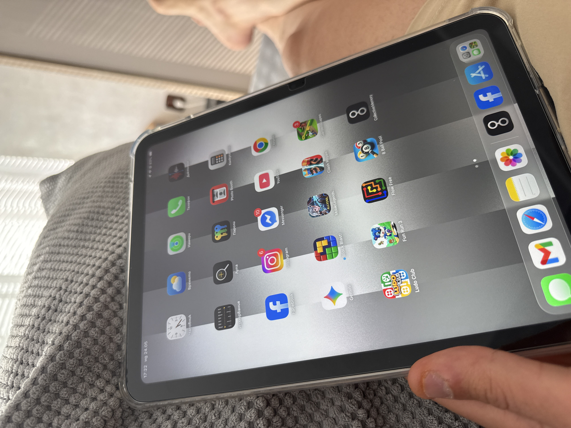 A person is holding an iPad in a clear protective case. The screen displays an array of application icons. Visible apps include "Telephone", "Instagram", "Facebook", "YouTube", "Chrome", "Ludo Club", "Fun Run 3", "Flow Free", and "8 Ball Pool", among others. The iPad rests against a grey, textured fabric, likely a cushion or blanket. Part of a hand is visible at the bottom right of the image. The lower left corner of the screen indicates the time as "17:22" and the date as "Hg 24.05." The location in the city of Lovech, Bulgaria is not identifiable in the image.
