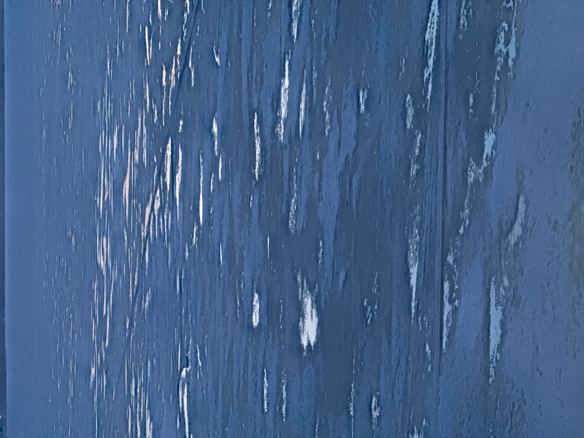 The image depicts a close-up of a textured blue surface, possibly a wall or door. The surface has vertical streaks of lighter blue and white, appearing as weathered or peeling paint. There are no people, subjects, or actions visible. The environment suggests an indoor or sheltered location. The image does not provide any information about the city of Votkinsk, Russia.
