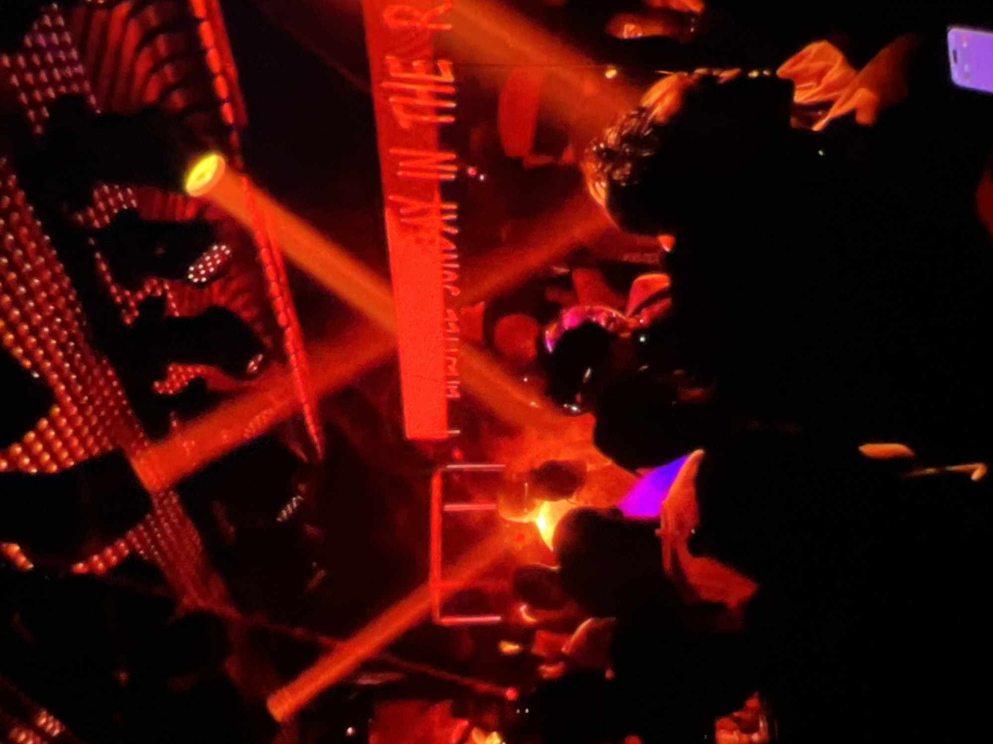 The image depicts a crowded nightclub scene illuminated by vibrant red and yellow lighting, likely in Lagos, Nigeria. A large, illuminated sign reading "FUN IN THE S..." is visible in the background, hinting at entertainment or a party. The foreground is filled with silhouettes of people, suggesting a lively atmosphere. Red spotlights crisscross the scene, creating dramatic beams of light. The overall impression is one of a dark, energetic, and possibly upscale venue.