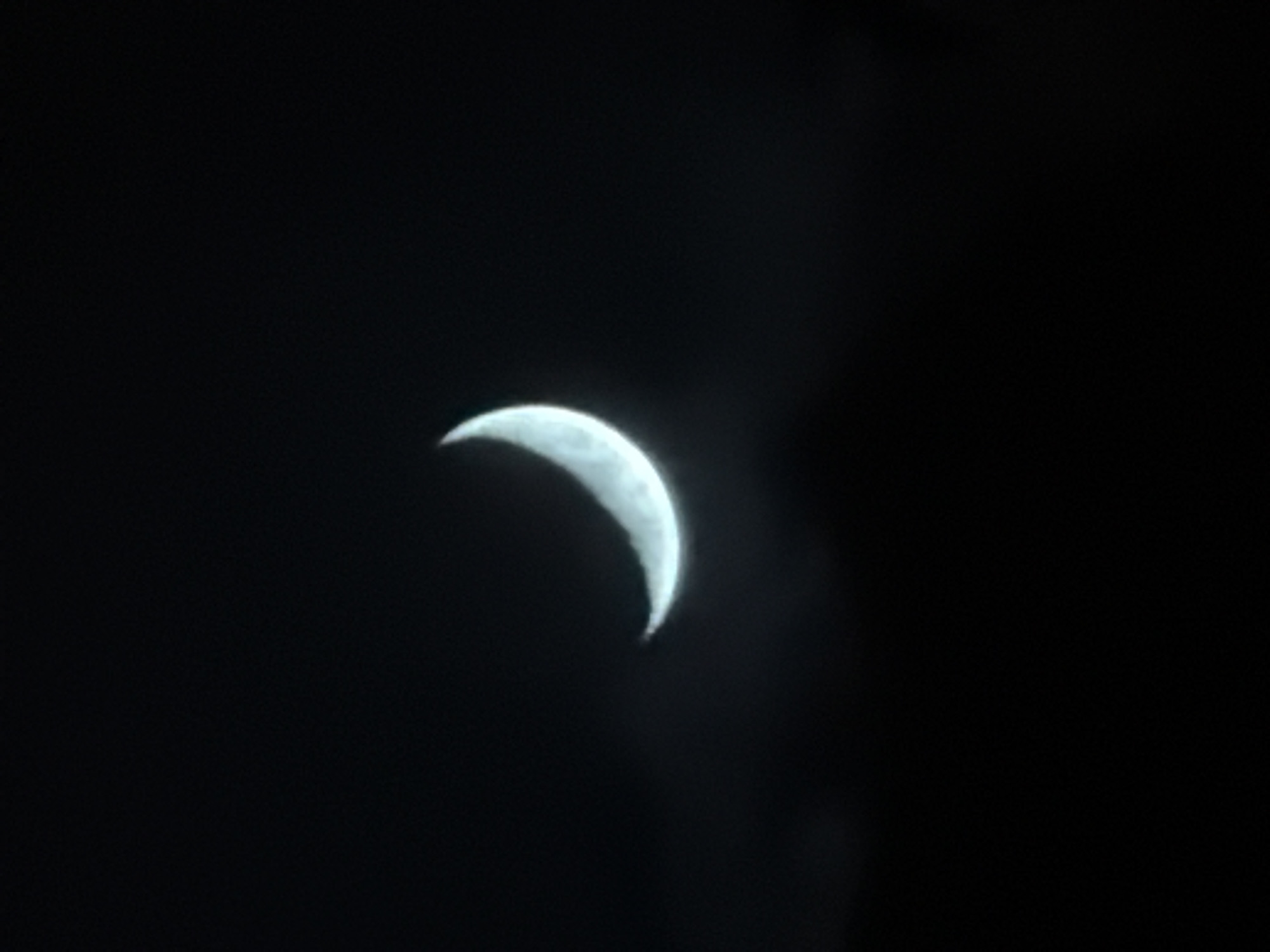 The image shows a crescent moon against a dark sky. The photo was taken in Tbilisi, Georgia. The scene is simple, with no other visible elements besides the moon and the dark sky. There is no indication of specific location or time.