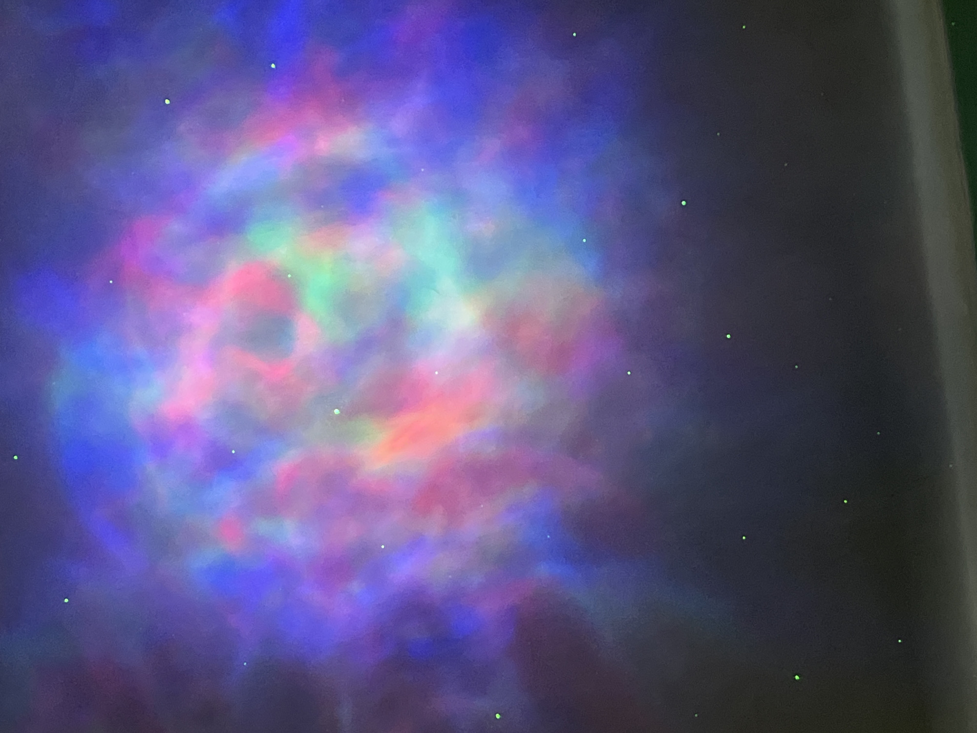 A colorful nebula-like projection with green dots resembling stars is displayed on a dark surface. There is no indication of this image being located in Nizhny Tagil, Russia, or any other city. The scene consists of a projected light pattern with no identifiable people, objects, actions, or interactions.