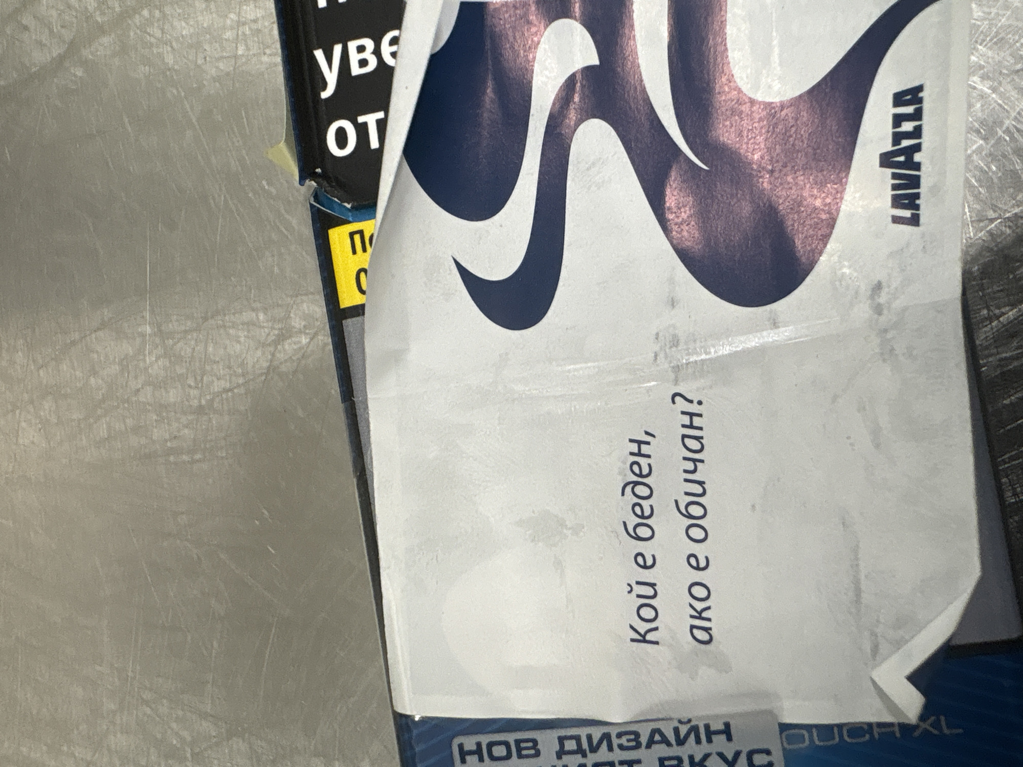The image shows a close-up of two overlapping packages, likely cigarettes. The package in the background has the letters "уве" (Uve) and "от" (Ot) and a yellow rectangle with "П" (P) and "C" (S) in black. On top of it is a Lavazza package with a large white logo and the text "Кой е беден, ако е обичан?" (Who is poor if loved?) and "НОВ ДИЗАЙН" (New Design). The image doesn't provide enough information to determine the exact location in Veliko Tarnovo, Bulgaria.