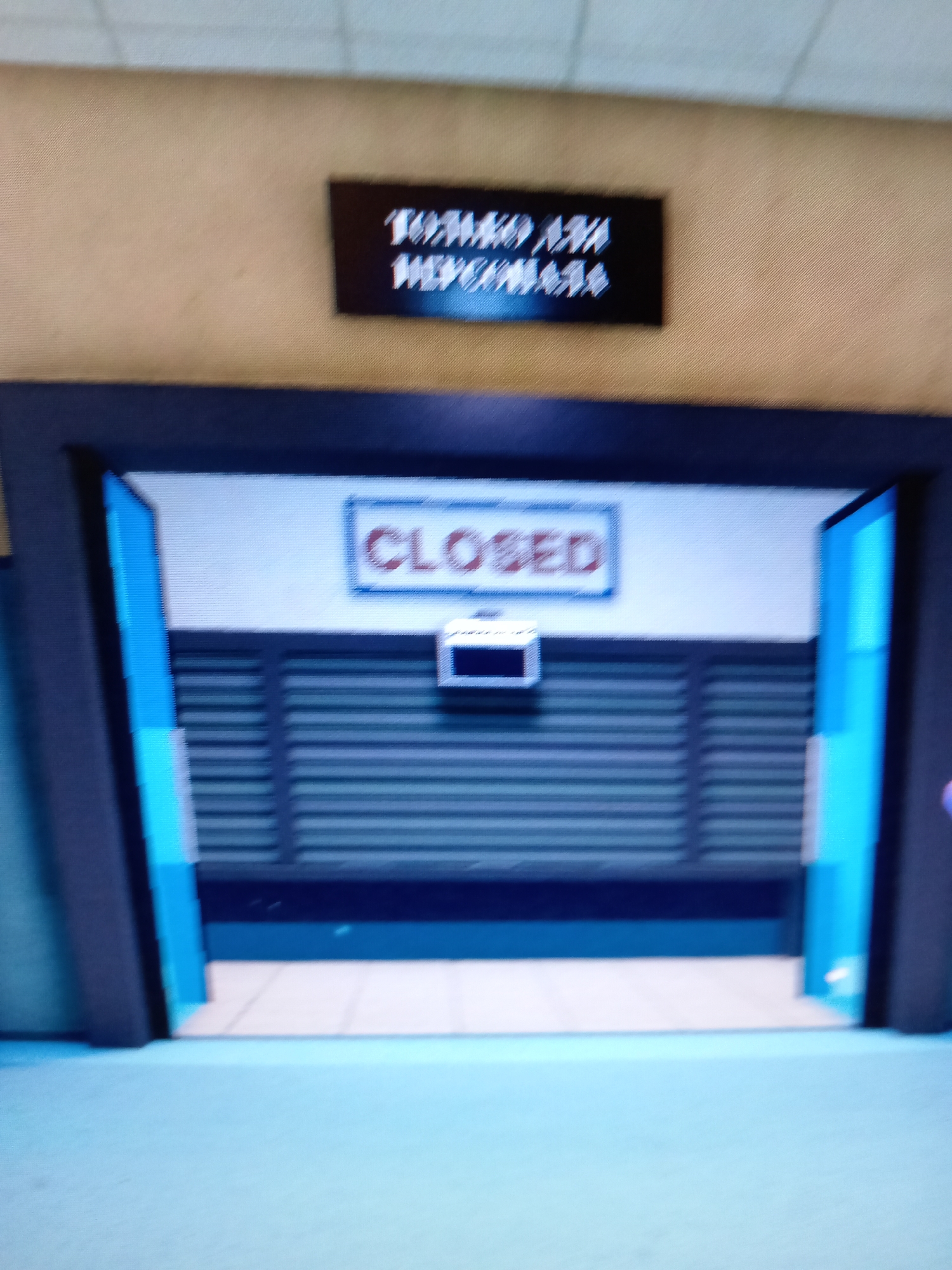The image depicts a digital rendering of an interior scene. A dark doorway frames a closed metal grate. Above the grate, a sign reads "CLOSED" in red text within a white rectangle. On the wall above the doorway, a black sign with white text is visible, but the text is illegible due to blurriness. The environment appears to be an indoor public space with light-colored walls and a floor. The overall aesthetic suggests a video game or digital simulation rather than a real-world photograph. There is no discernible information about the location in the city of Rudny, Kazakhstan.