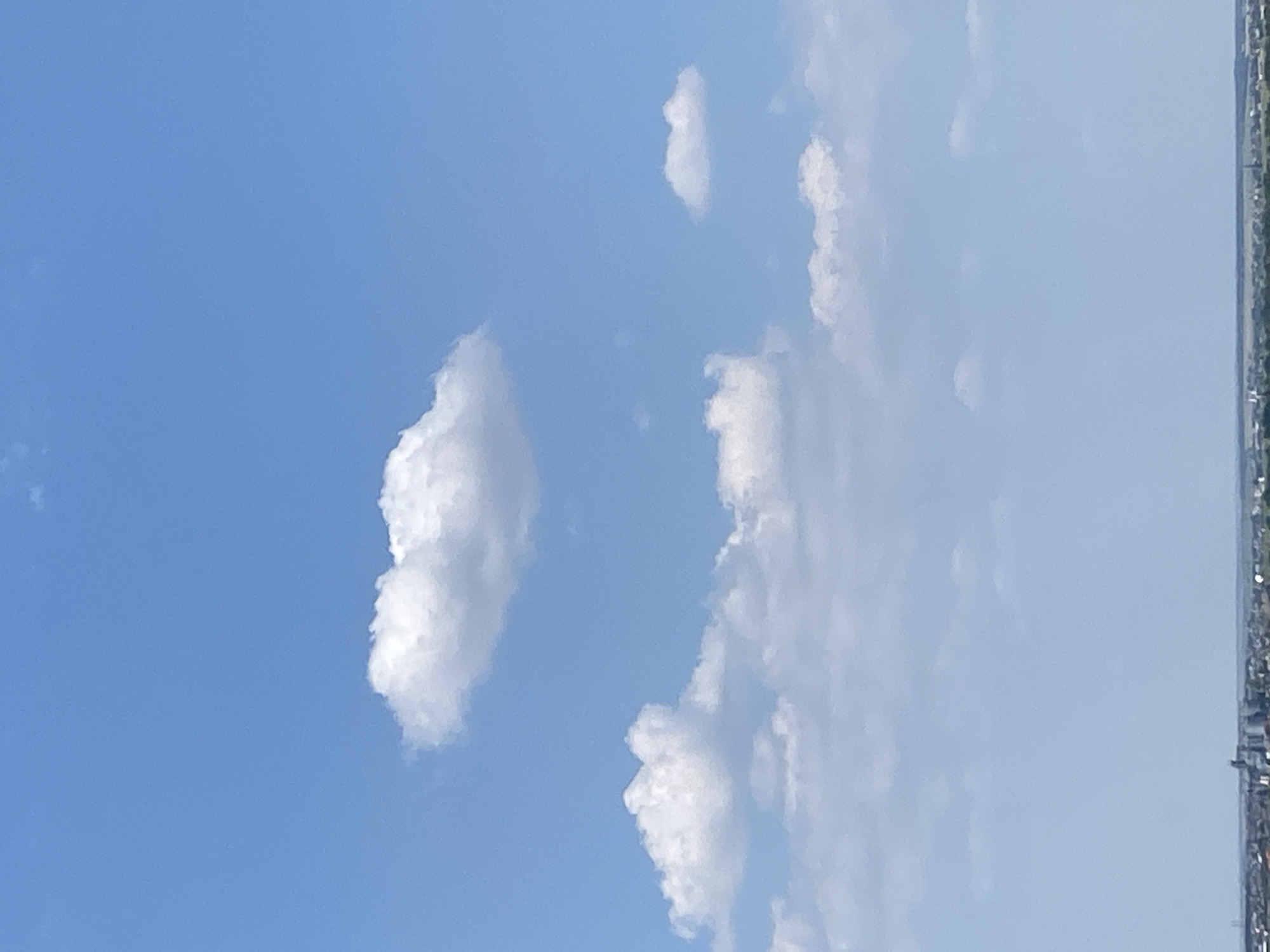 A slightly overcast, bright blue sky is visible, with scattered cumulus clouds. The lower portion of the image shows a distant, hazy horizon line, suggesting a cityscape or developed area. This is a view from the city of Chornomorsk, Ukraine.