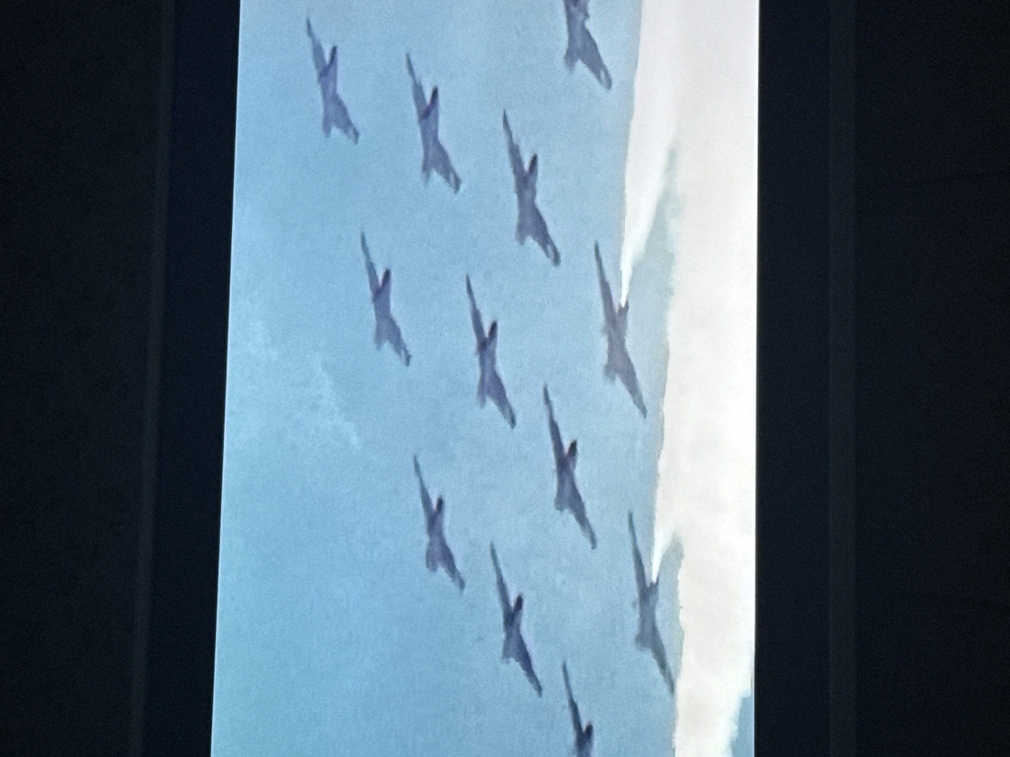 The image shows a photograph of a framed artwork or picture displayed on a wall. The artwork features a sky blue background with several abstract, bird-like shapes dispersed throughout the frame. The objects are predominantly light blue with soft, blurred edges, and there appears to be a cloud-like white space that goes down the right side of the painting. The photograph appears to be taken indoors.
There is no information that gives the location as the city of Mytishchi, Russia.