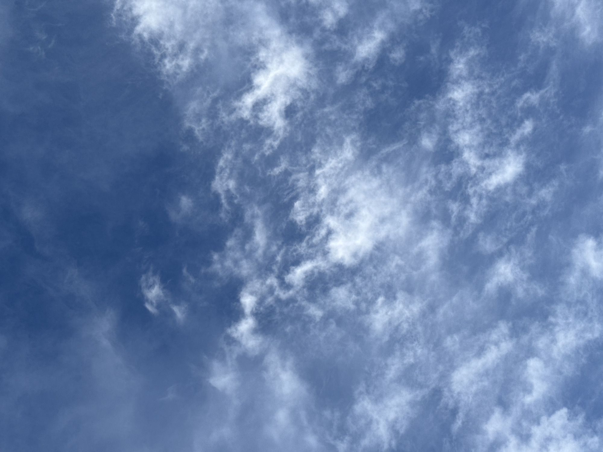 The image depicts a blue sky partially covered with thin, wispy white clouds. The clouds are scattered across the frame, with a higher concentration on the right side. There are no people, objects, or other subjects visible besides the sky and clouds. The location is unspecified.