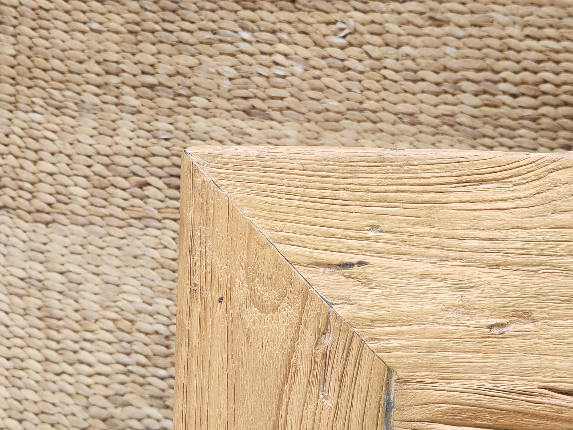 This close-up media file features a corner of a wooden object set against a woven, textured background. The wooden object appears to be made of light-colored wood with prominent grain lines and some darker imperfections, suggesting a rustic or natural aesthetic. The woven background is composed of many small, oval-shaped elements, tightly packed together, creating a textured surface that contrasts with the smoother wood. The lighting suggests daytime, possibly outdoors or in a well-lit indoor space, with no specific indications of weather. There are no people, text, or discernible activities taking place in the frame. The composition focuses entirely on the textures and materials of the two surfaces. The location context of Maitland, United States of America, does not provide specific visual cues within the image itself.