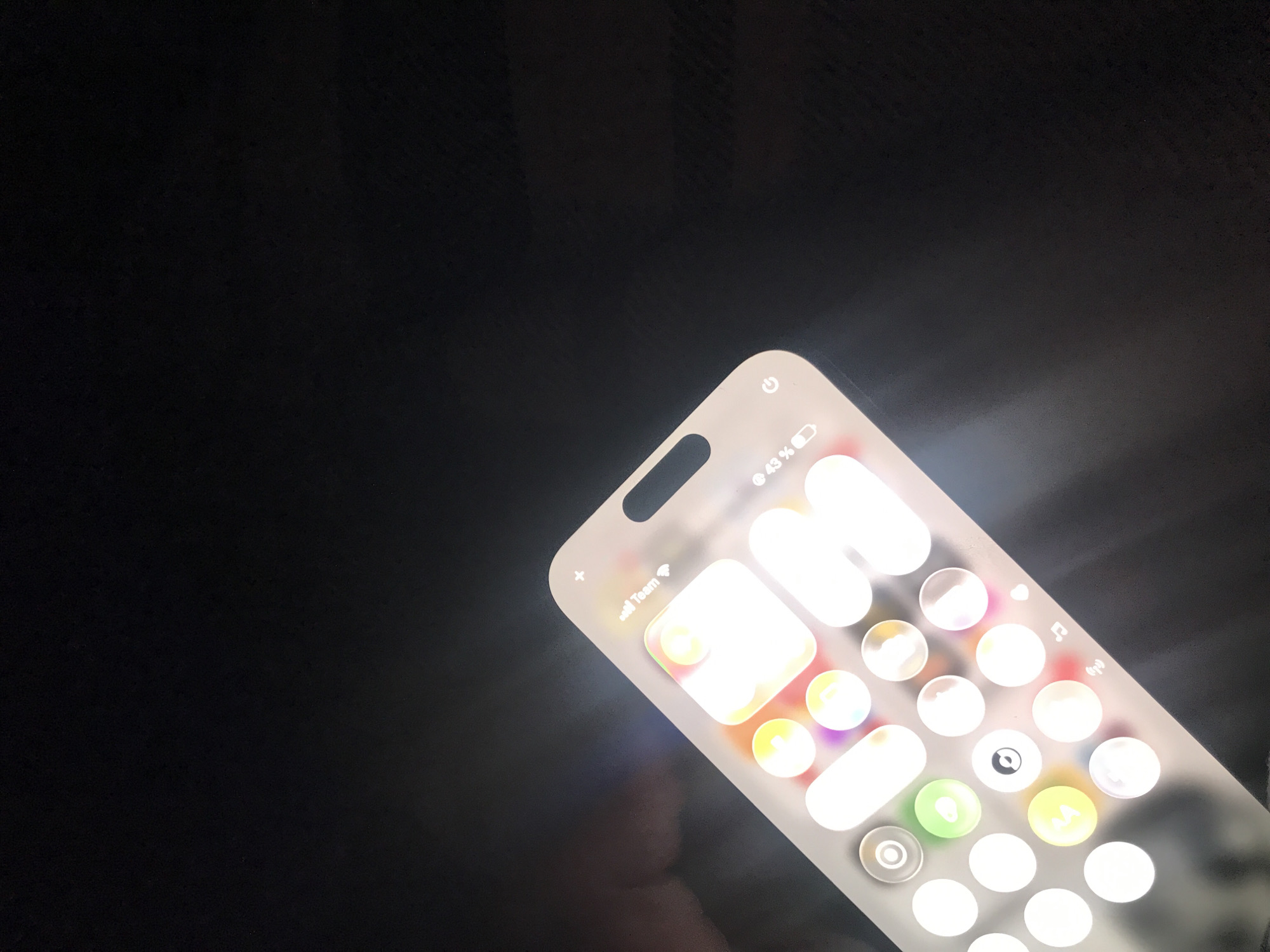 A brightly lit smartphone screen displaying the home screen is angled in the lower right of the frame. The screen shows multiple app icons. The battery indicator reads 43%. The background is a blurry dark surface. No people are clearly visible, but there is possibly a faint face in the reflection. No other details suggest the location is Yerevan, Armenia.