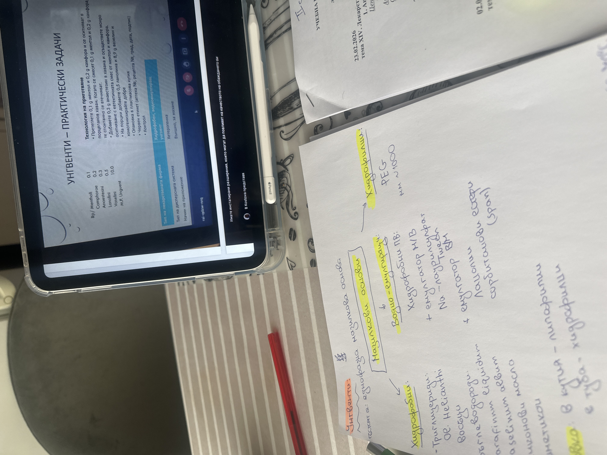The image shows a tabletop scene with study materials. An iPad displaying a Bulgarian text about ointments and practical tasks is placed on a striped surface. Adjacent to the iPad are handwritten notes in Bulgarian, organized into categories such as "hydrophobic" and "water-emulsifying." A red pen lies on the striped surface, and a white Apple Pencil is positioned to the side of the iPad. Additional papers with written text are visible in the background. The location is likely a personal study space, potentially in Sofia, Bulgaria, based on the Cyrillic script used in the documents.