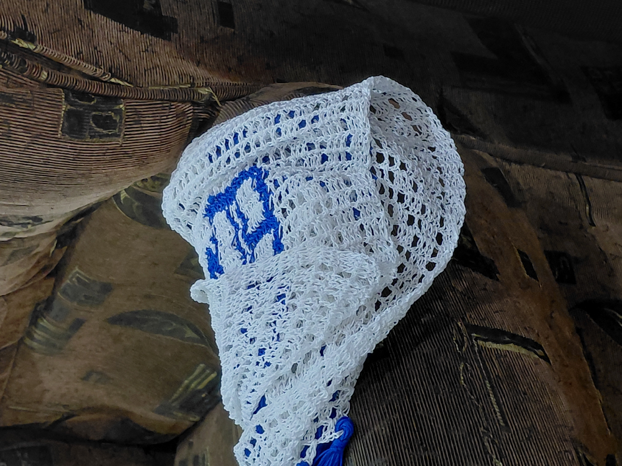 A white crocheted bag with blue accents is placed on the armrest of a brown, textured couch. The couch appears to be in a domestic setting, possibly a living room. The image is taken from a slightly elevated angle, focusing on the bag and a portion of the couch. The background is blurred, suggesting a shallow depth of field. There are no people or animals visible in the image. The specific location within Santa Ana, Venezuela cannot be determined from the visual information provided.
