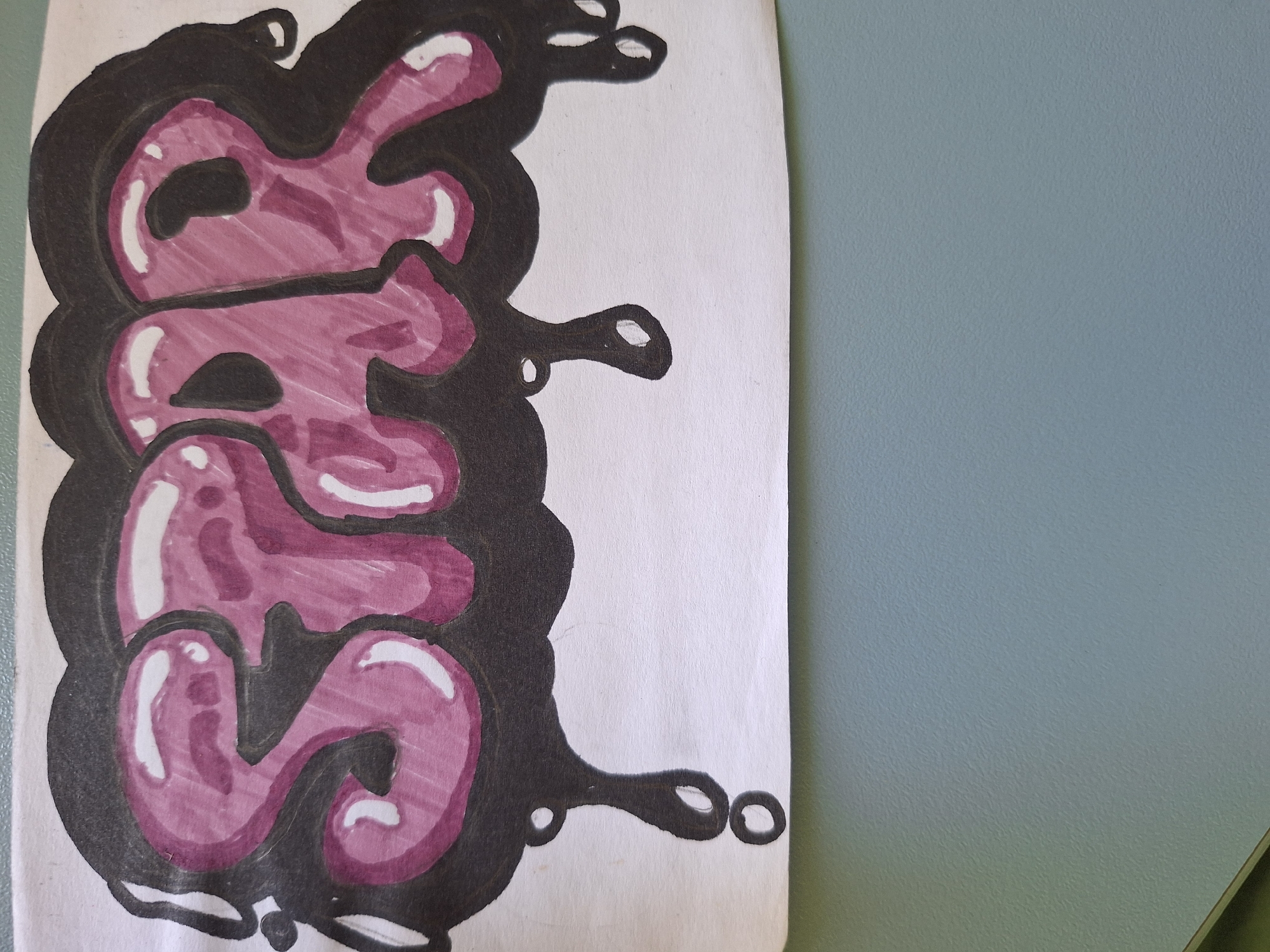 An artistic drawing of the letters "G", "R", and "S" is depicted in pink and black marker on white paper. The letters are stylized in a graffiti bubble-letter format, with thick black outlines and a glossy pink fill, accented with white highlights to give them a 3D effect. The drawing is set against a plain white background, with a portion of a light blue textured wall visible to the right of the paper. The image does not contain any identifiable landmarks or specific details that would allow for pinpointing a location within Varna, Bulgaria.