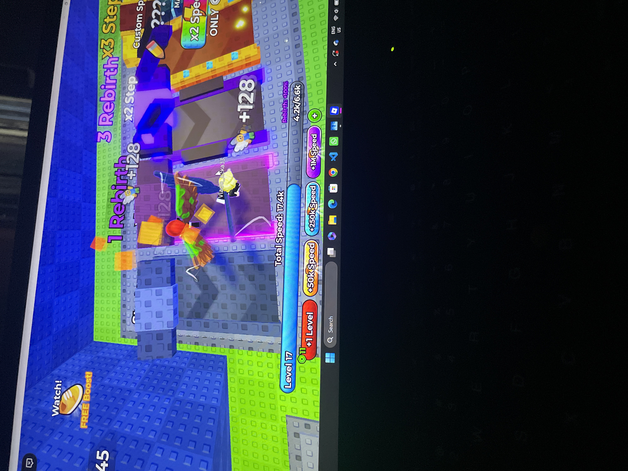 The image shows a screenshot of a video game, likely a Roblox game, displayed on a computer screen. The game appears to be a simulator where players can gain levels, speed, and rebirths. In the foreground, a laptop keyboard is partially visible, with the screen reflecting on the keys. The game interface features elements like "Level 17," "+1 Level," "+50k Speed," and "+1M Speed." There are also indicators for "Rebirth" and "Speed" with numerical values. The in-game environment is colorful and blocky, characteristic of Roblox games, with blue, green, and purple elements. The user's cursor is visible on the screen, hovering over a "Search" bar in the Windows taskbar at the bottom. There are no specific landmarks or elements in the image that can be used to determine its location in Iyafin, Nigeria. The scene depicts a digital environment within a video game, not a real-world location.