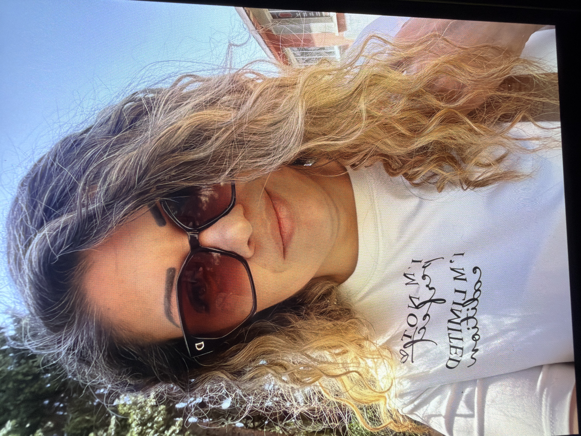 A photograph depicts a person wearing sunglasses and a white T-shirt with black writing, outside against a background of foliage and sky. The writing on the shirt reads "I'm not limited." The photo appears to be taken outdoors, with natural light illuminating the subject. The precise location within Dryanovo, Bulgaria is not discernible from the image.