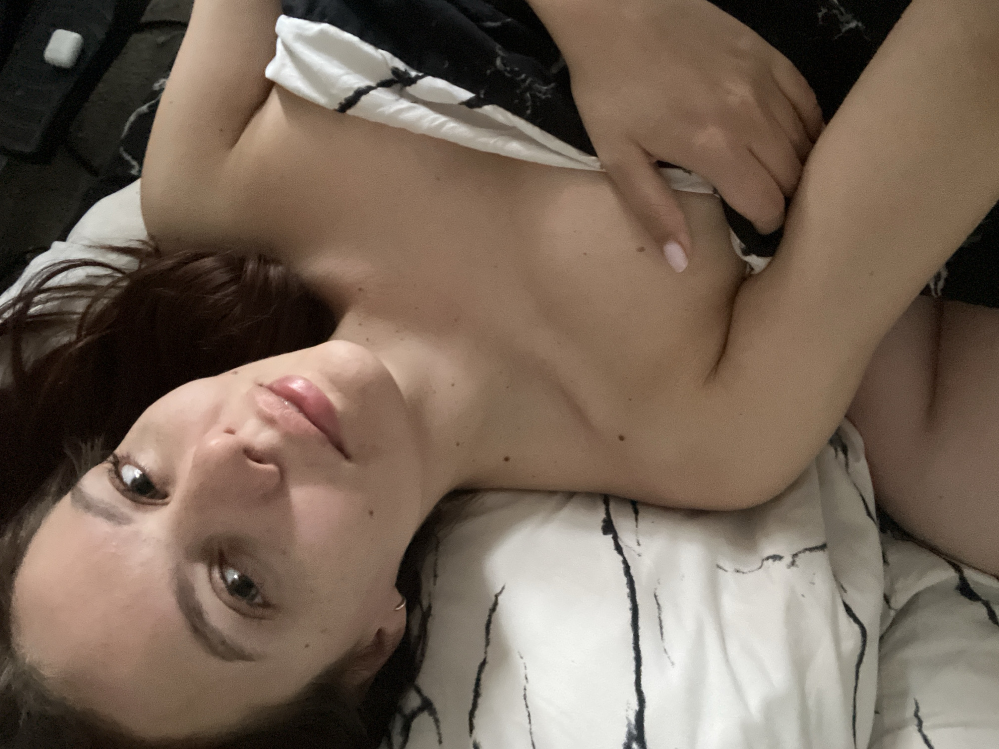 A woman is lying on a bed. She is partially covered by a black and white striped blanket. The woman is facing the camera. She has brown hair and brown eyes. The setting is indoors. There is not enough information to verify the location in Chaikovsky, Russia.