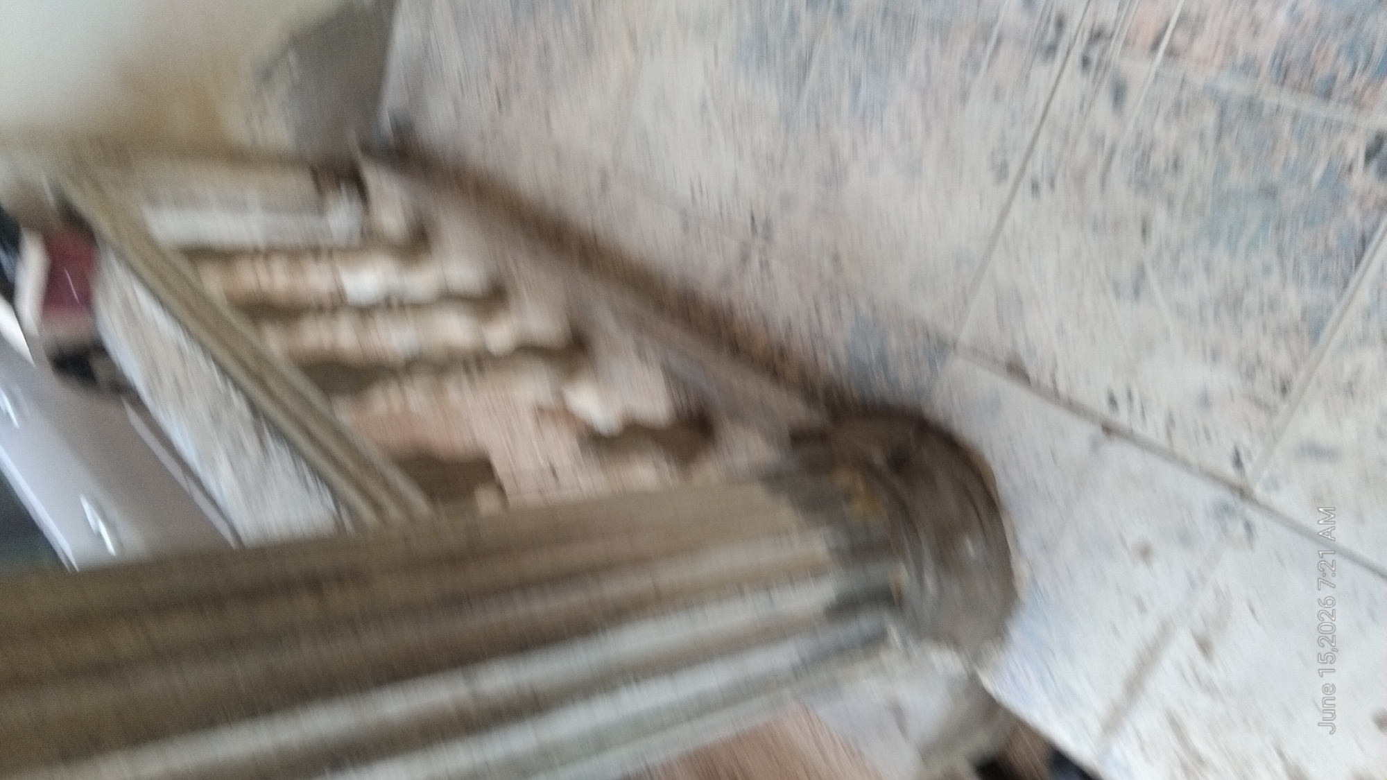 The image shows a blurred view of a staircase with a concrete railing and tiled flooring. A portion of a light-colored vehicle is visible in the background, and a red object, possibly a box, is on top of the railing. The timestamp in the bottom left corner indicates "June 15, 2026 7:21 AM". The image is taken in a residential or public outdoor setting, likely a stairway leading to a building. The scene appears to be in Howayi, Nigeria.