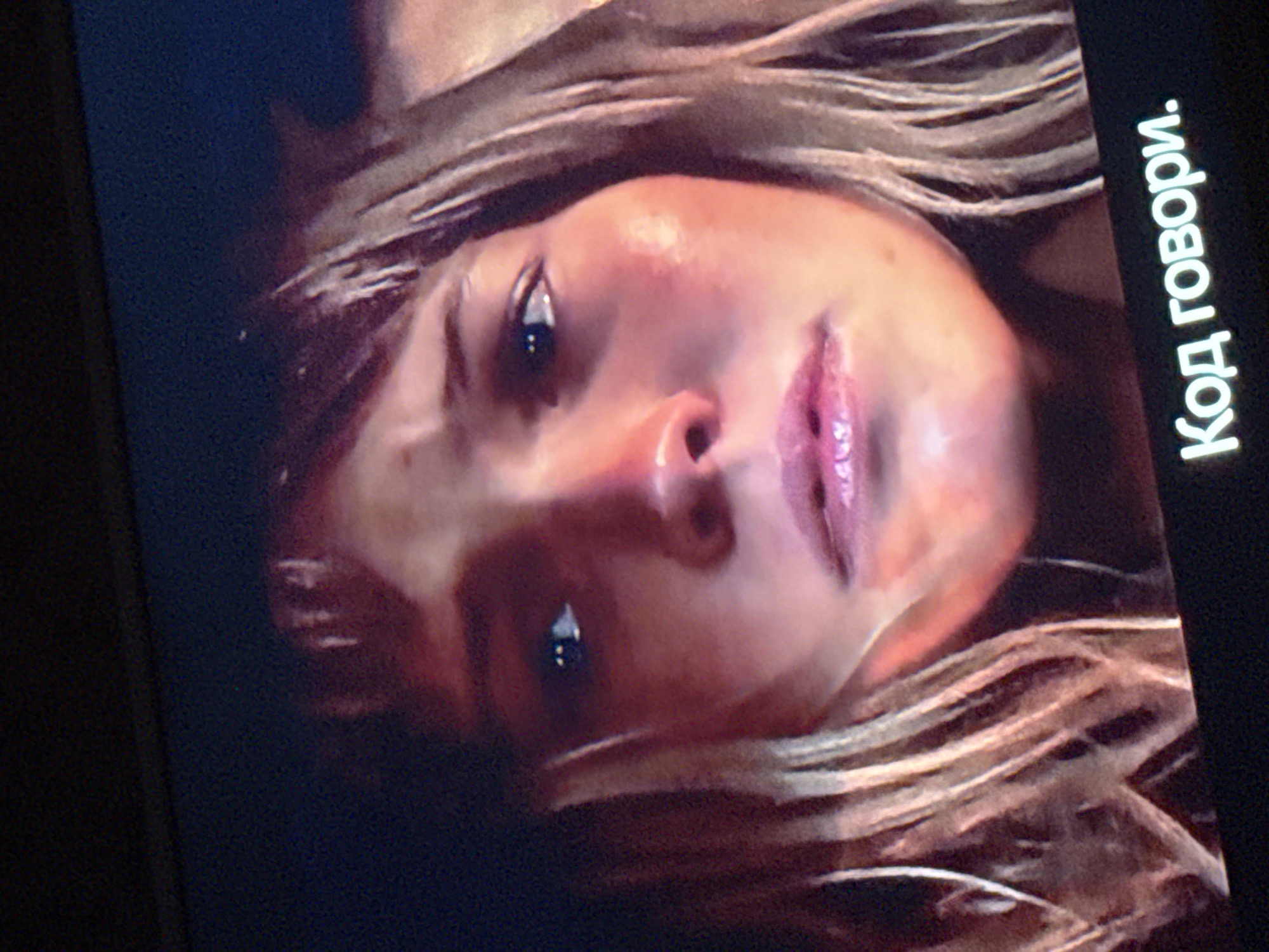 The image shows a close-up of a fair-skinned person's face, possibly female, with light blonde hair. The individual is looking upwards and to the side. The image appears to be a still from a screen, with the text "Код говори." visible, which translates to "Code, speak." in Russian. The photograph was not taken in Mytishchi, Russia.
