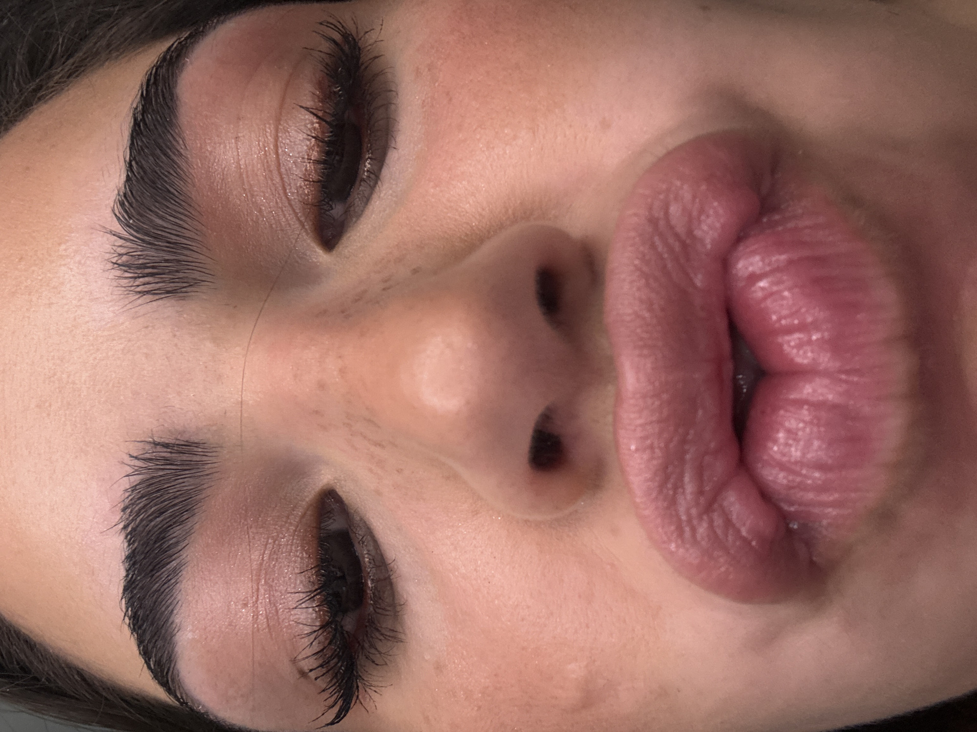A close-up, slightly angled shot depicts a person's face, focusing on the eyes, nose, and exaggeratedly pursed lips. The person has groomed eyebrows and appears to be wearing eye makeup and false eyelashes. The skin tone is fair with visible freckles. The lips are a rosy-red color. The photo does not offer any details allowing it to be placed in San Bernardino Tlaxcalancingo, Mexico.
