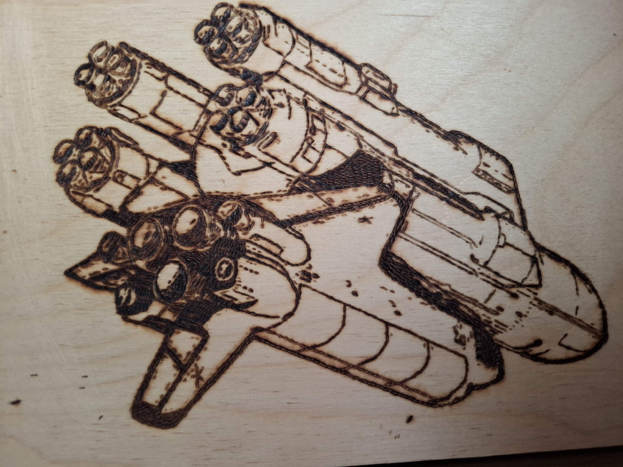 A wood burning artwork on a light-colored wooden board depicts a spaceship or futuristic vehicle. The artwork consists of various cylindrical and rectangular shapes connected to form the overall structure of the spacecraft. At the front of the spacecraft are several large, circular engines or thrusters with multiple nozzles, while the central portion features a more complex arrangement of panels, tubes, and other mechanical details. There is no indication of any people, actions, or interactions within the image. There is no evidence of the location of Амзя, Russia.