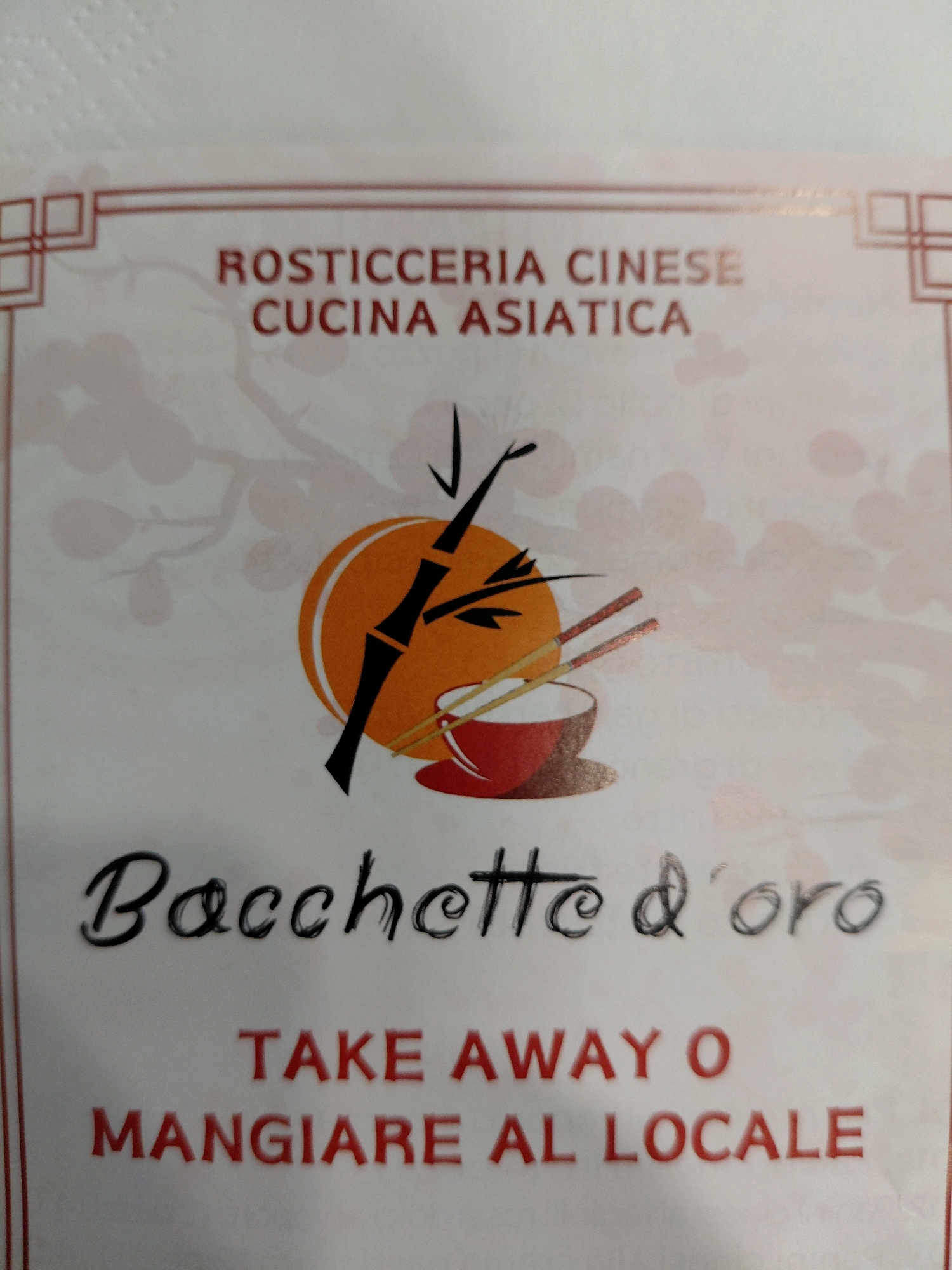 A menu from a Chinese restaurant features the text "ROSTICCERIA CINESE CUCINA ASIATICA" at the top, followed by the restaurant name "Baguette d'oro" below a graphic of bamboo stalks, a bowl, and chopsticks. At the bottom, the menu also indicates "TAKE AWAY O MANGIARE AL LOCALE." The background of the menu has a subtle pattern of light pink circles and branches. The image is a close-up of the menu, with no people or specific location details visible.