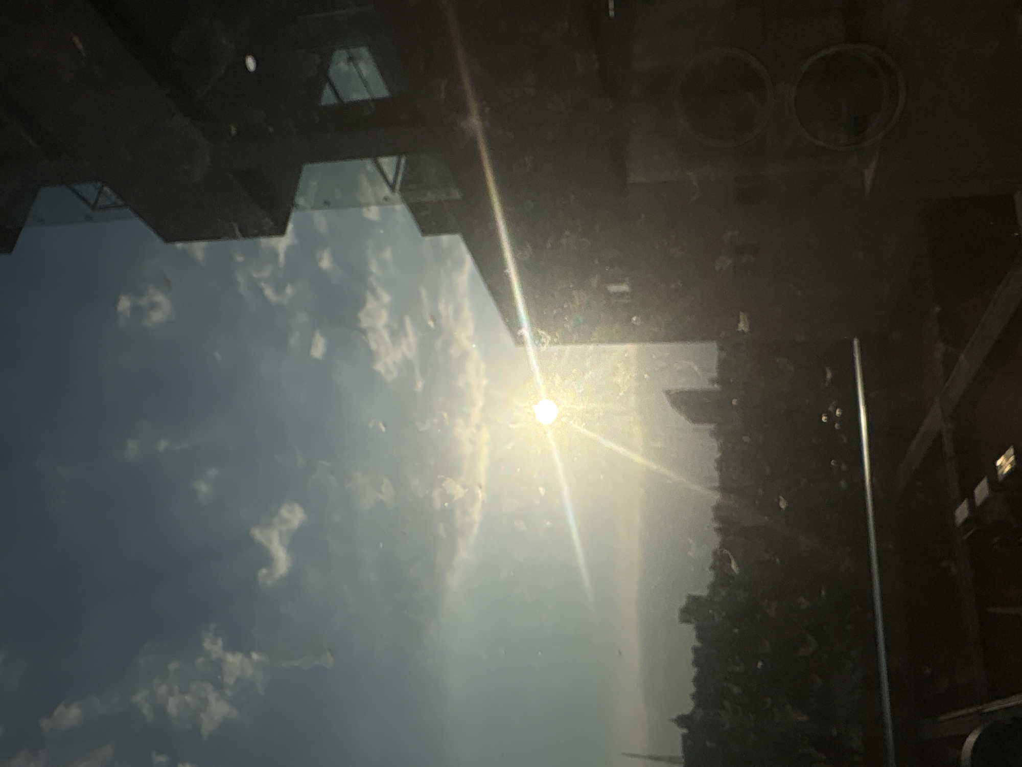 The image shows a reflection in a dirty window. The reflection is of the sky with clouds and the sun. The reflection also includes the silhouette of a building and possibly a cityscape. It is difficult to discern specific details or pinpoint the location in Puebla, Mexico, without further context or visual markers.