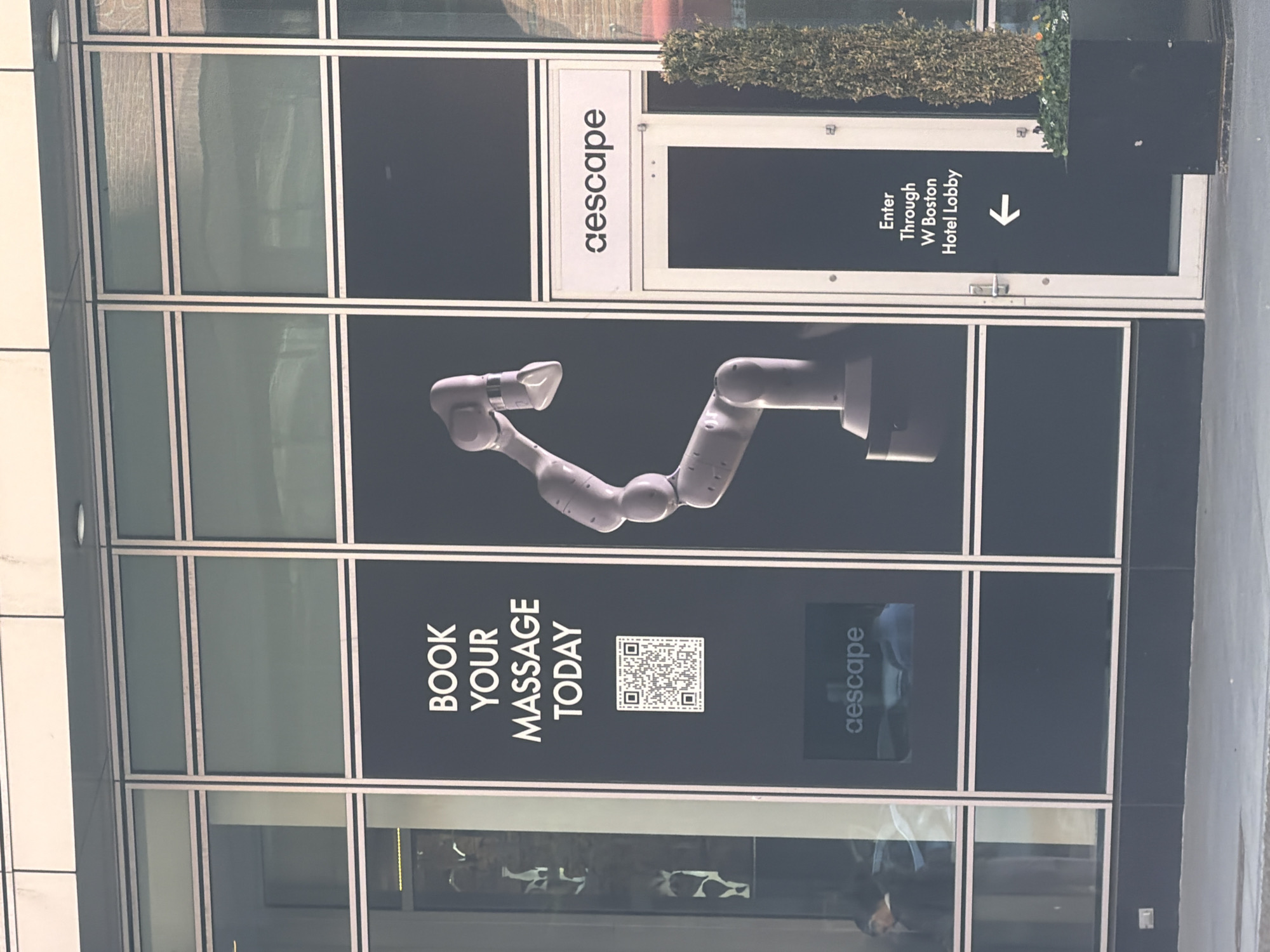 The image shows a store sign in Boston, United States. The sign advertises "aescape" robotic massages. The sign says "Book your massage today" above a QR code, and includes the words "Enter through W Boston Hotel Lobby" along with an arrow.